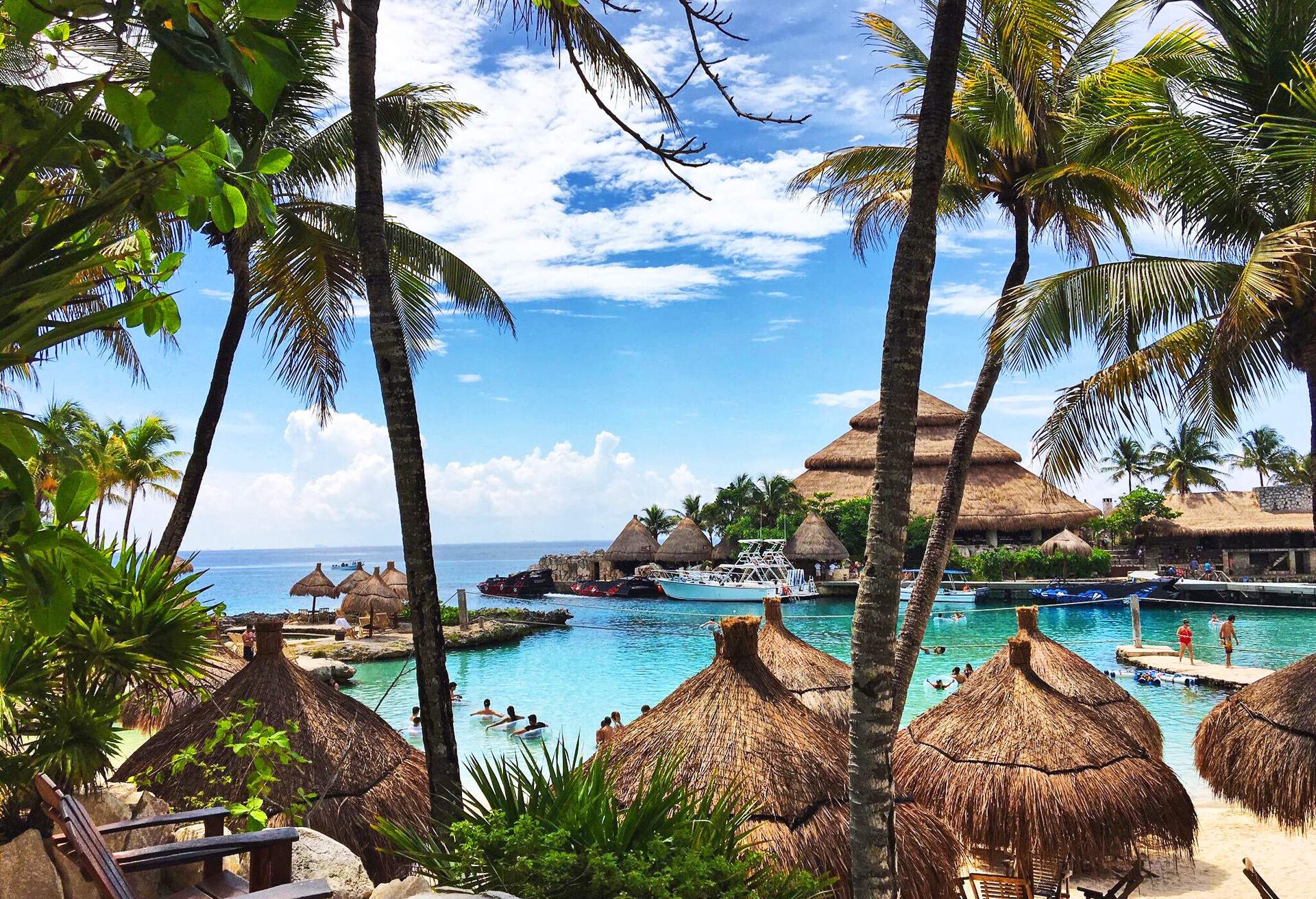 Several tourists are on a small beach surrounded by thatch umbrellas.