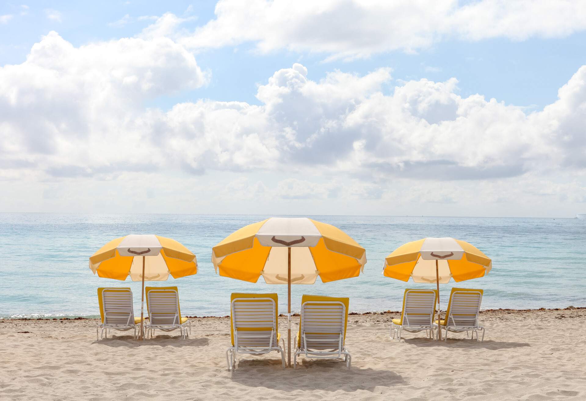 Yellow and white striped beach umbrellas and sun loungers strewn on the sand towards the sea.
