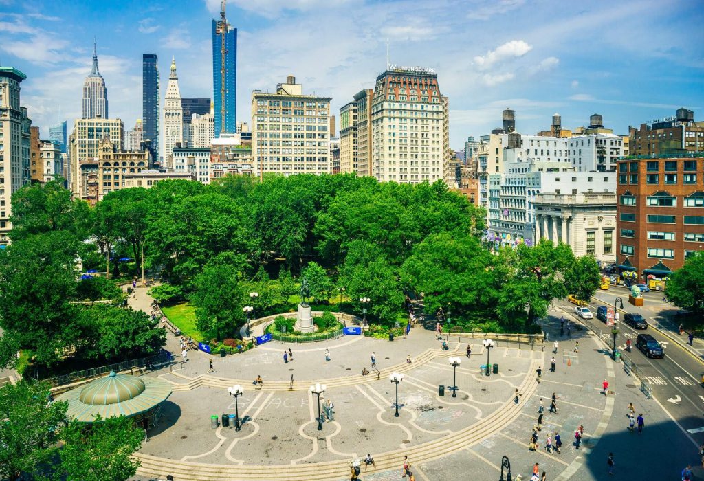 View of a square with high buildings and green trees in New-York City