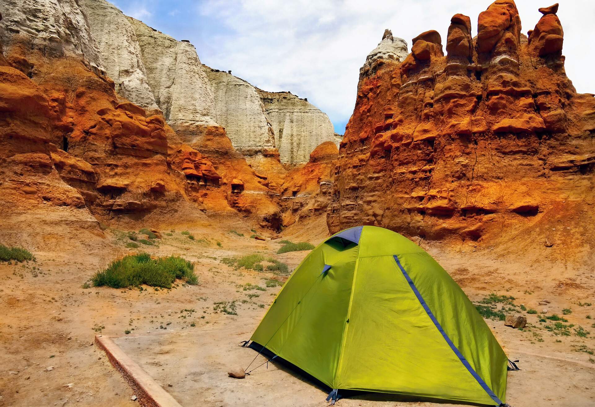 Green tent located at the base of a colourful valley with eroded and unique sandstone rock formations.
