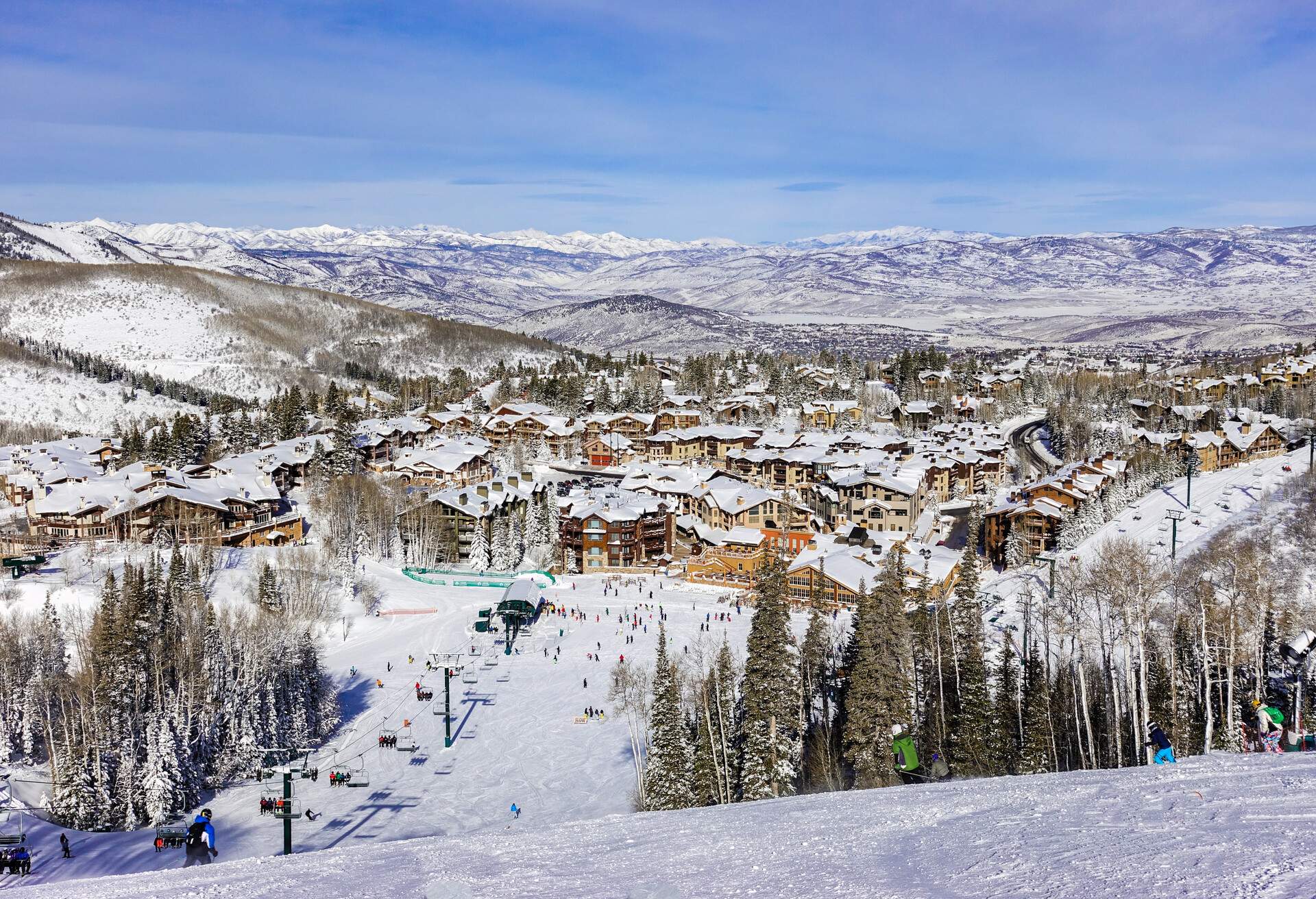 A ski slope with a view of the ski village's urban setting and the crowded ski lift station.