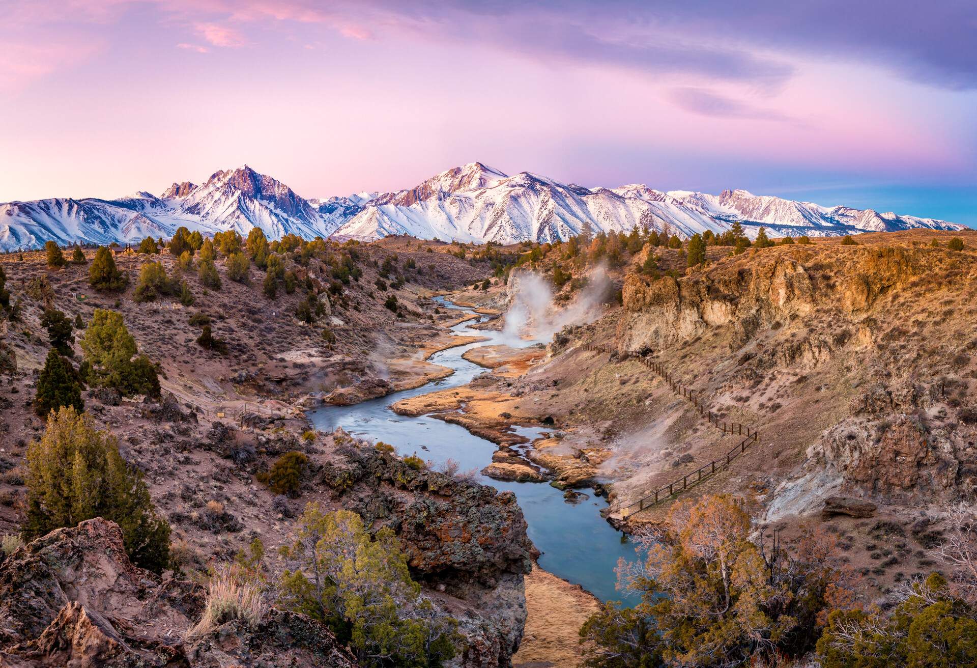 A creek meandering through a dry land bordered by a snow-covered mountain range.