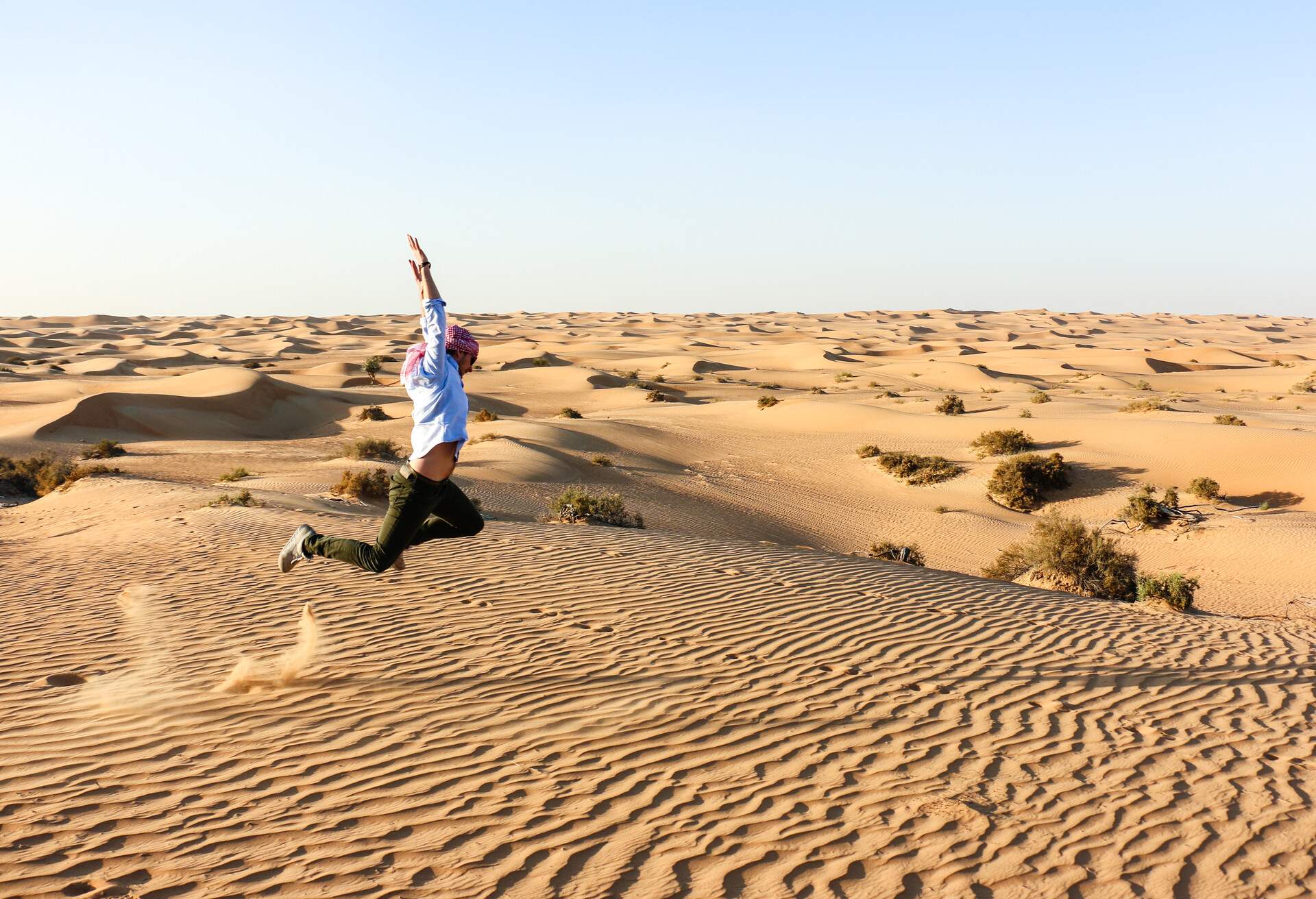 A male tourist jumps with raised hands in the middle of the desert.