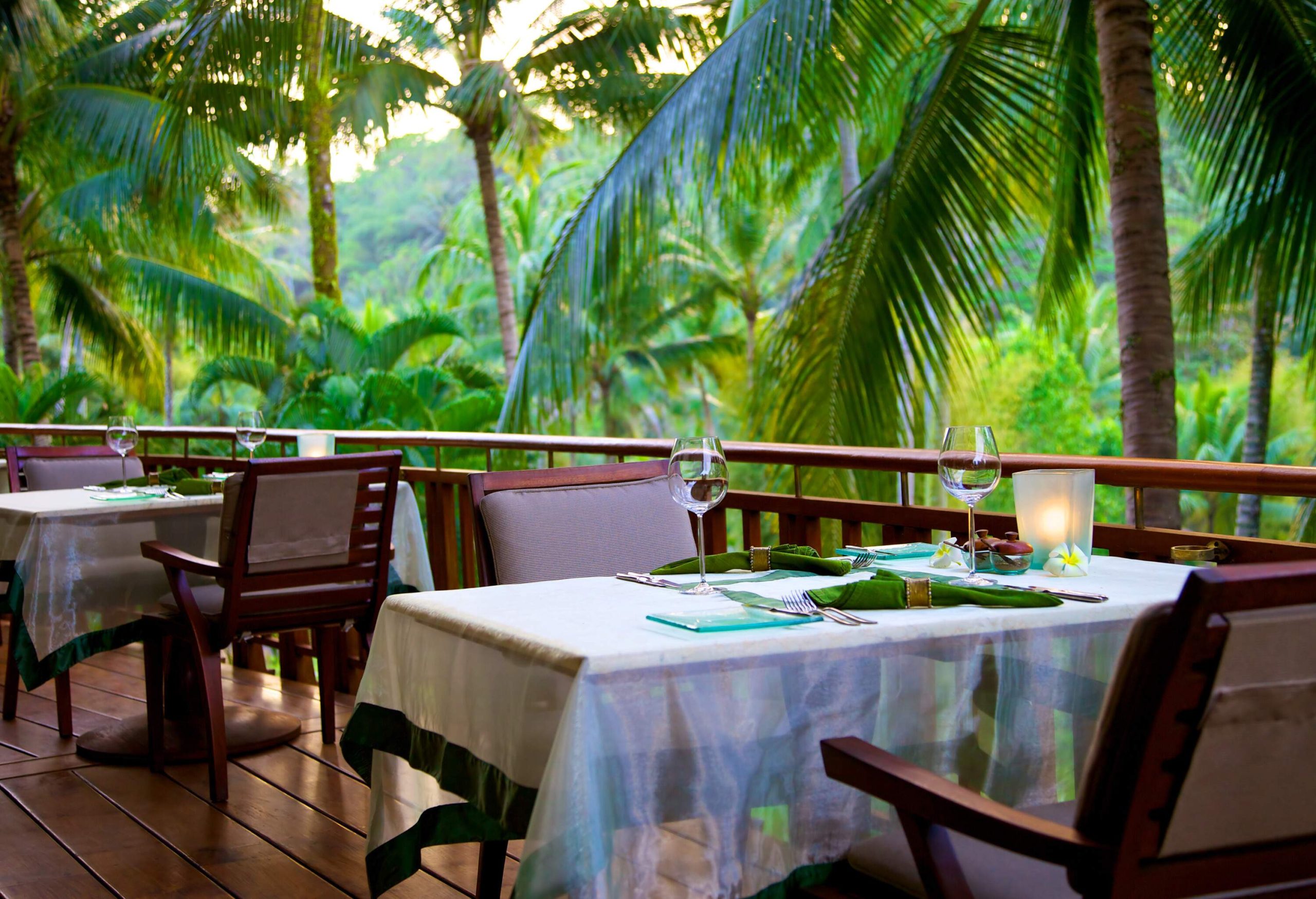 Tables and chairs on a wooden deck surrounded by lush green forest.
