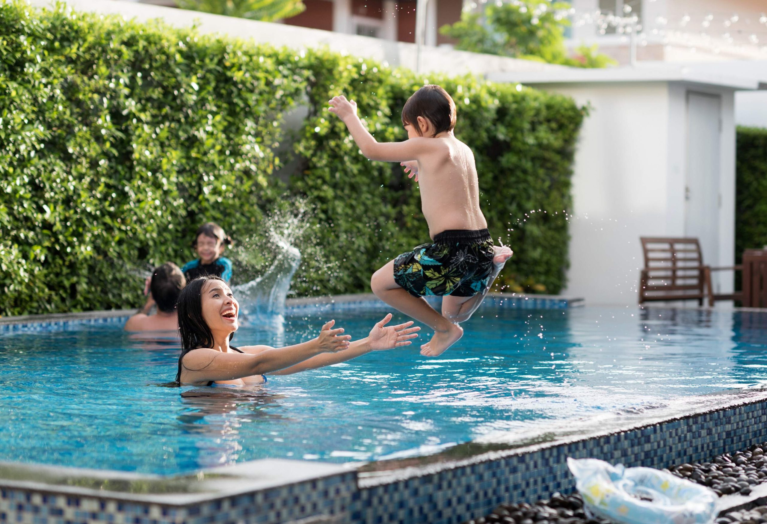 A mother waiting to catch her son as he jumps into the pool.