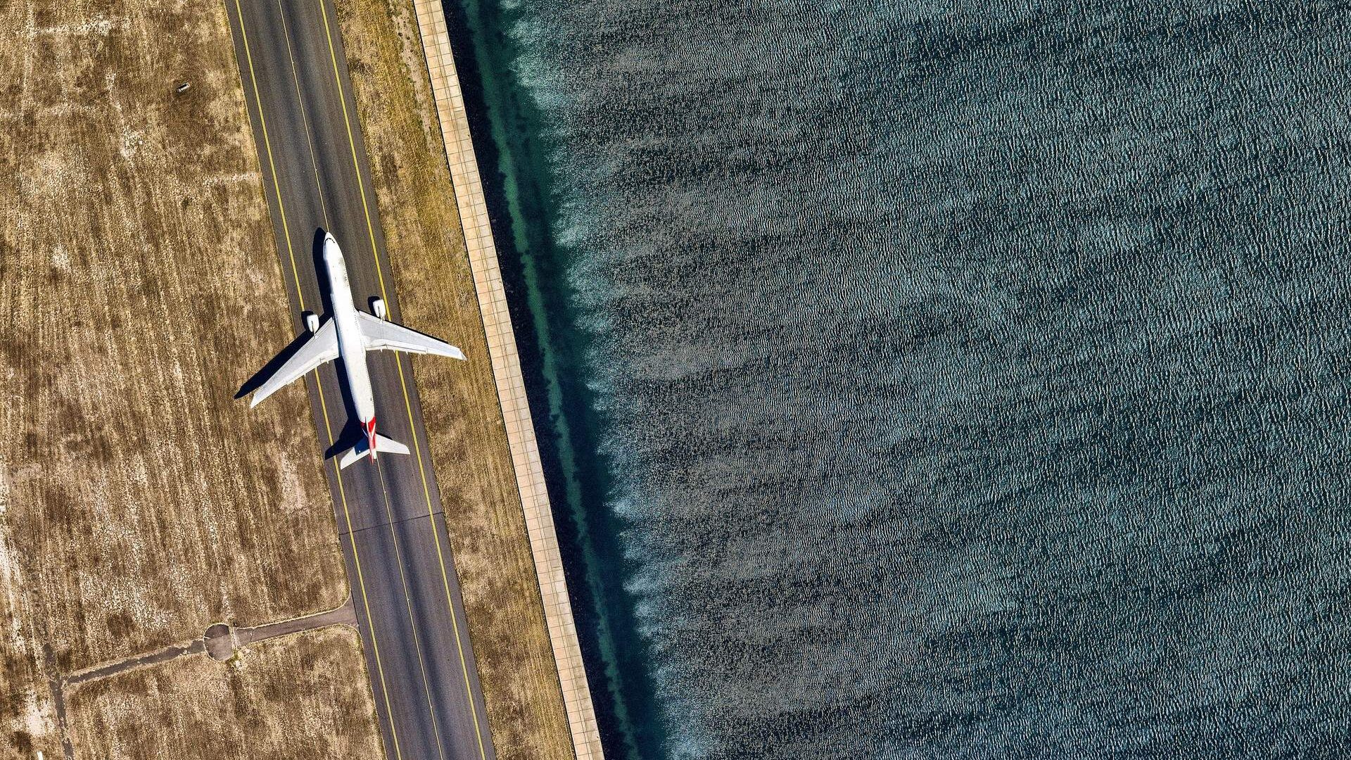 A white airplane on the runway alongside the ocean.