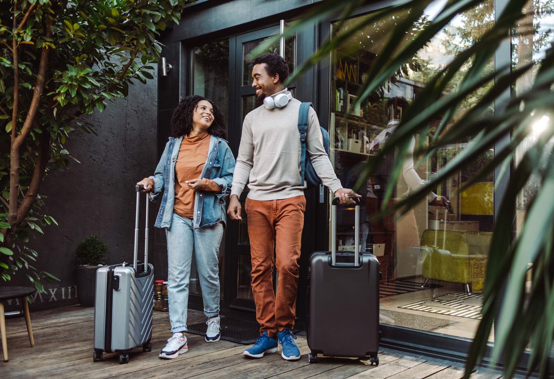 A young couple standing at the building entrance with their suitcases.