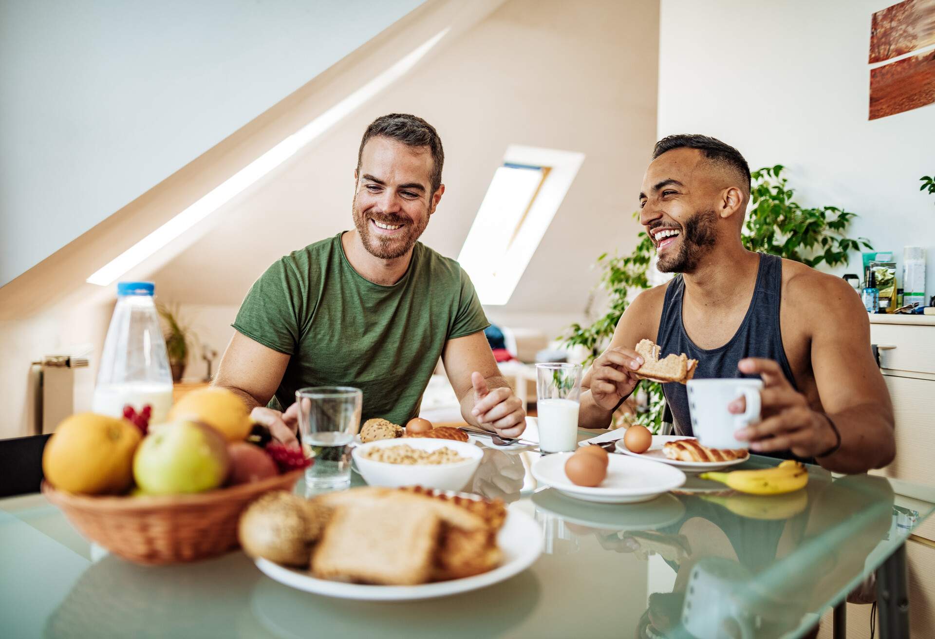 A gay couple shares a joyful breakfast at home, laughing and cherishing each other's company.