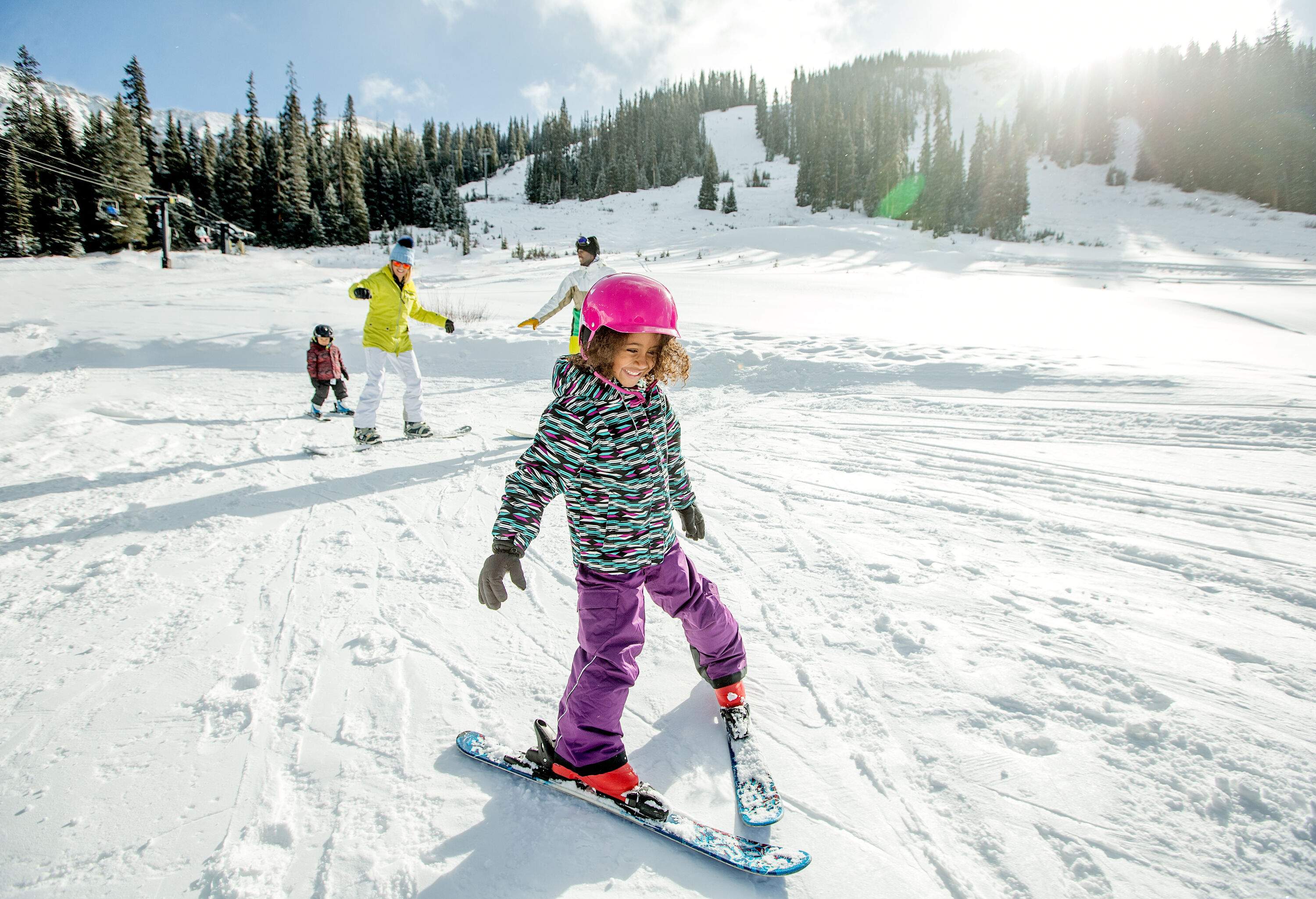 A little girl skiing with caution with people trailing behind her in a snowy woodland.