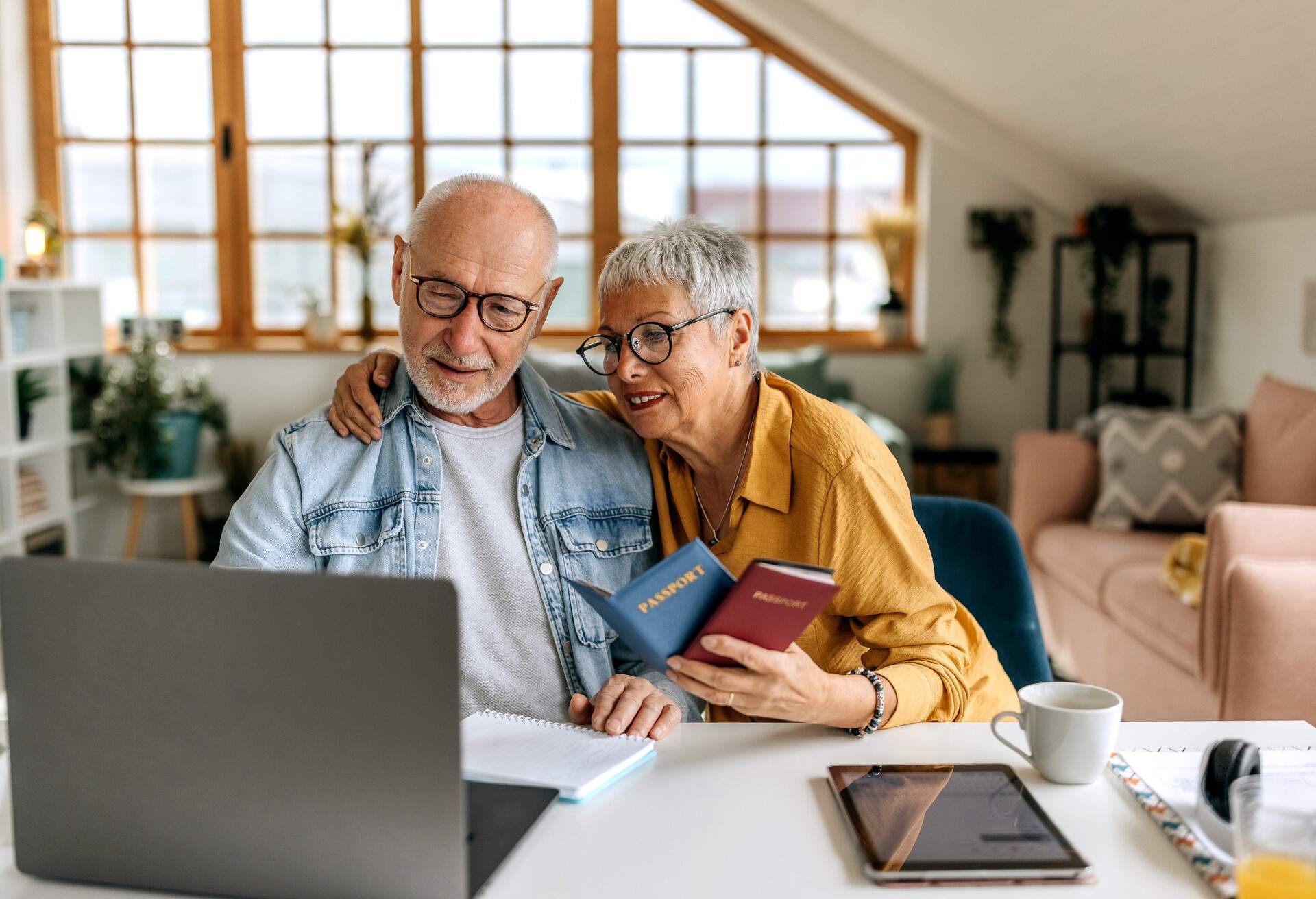 Senior couple sitting at a table in front of their laptop and booking a flight