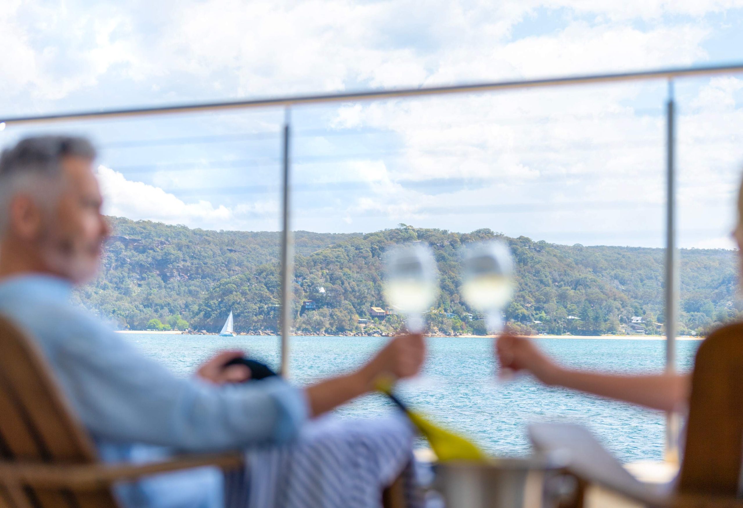 Mature couple drinking wine out on the deck. They are happy and smiling sitting in deck chairs. The sea is in the background. Focus on the background