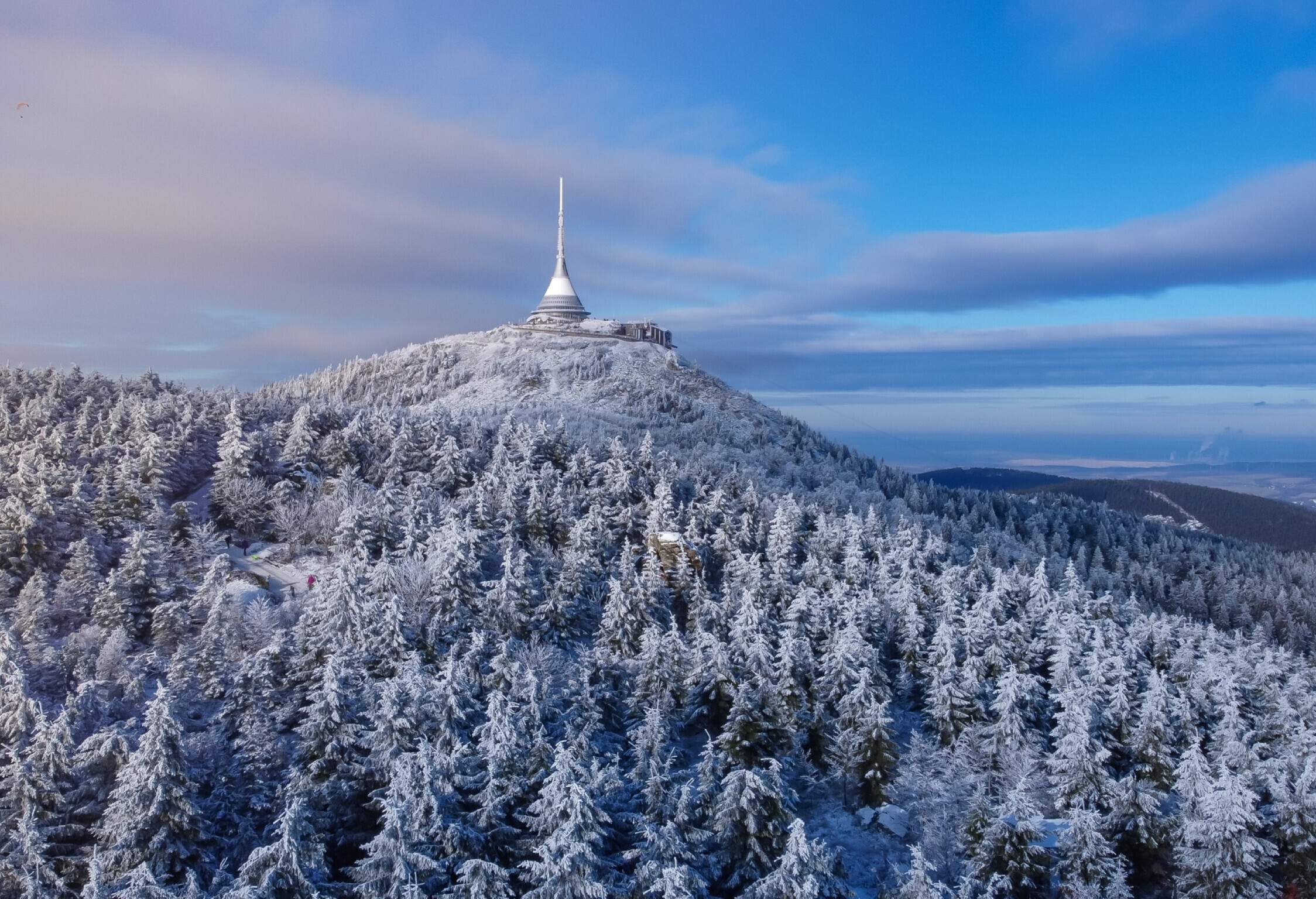 Snow-covered cypress trees surround the tower on the mountaintop.