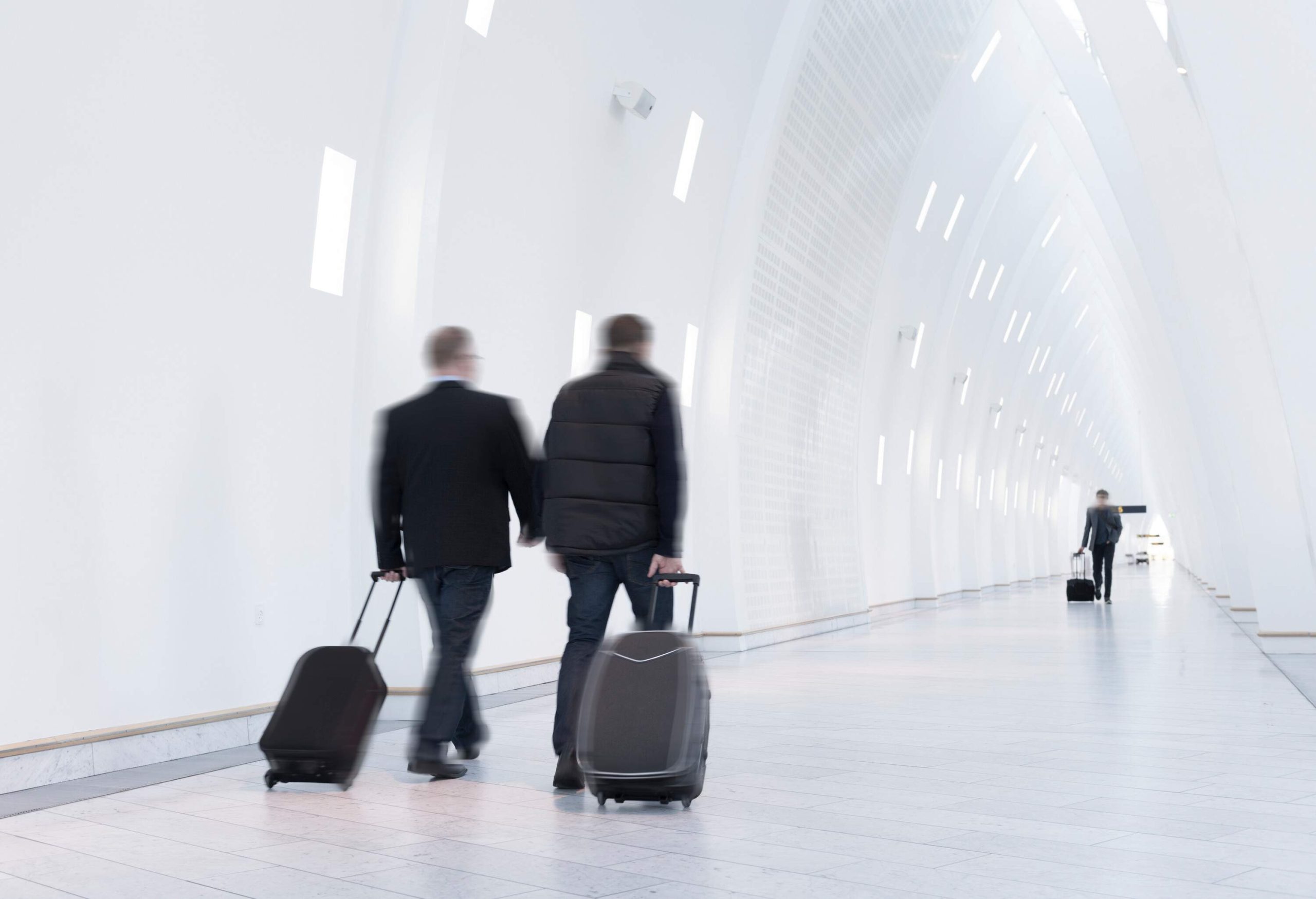 Three people with suitcases walking through a pristine hallway.