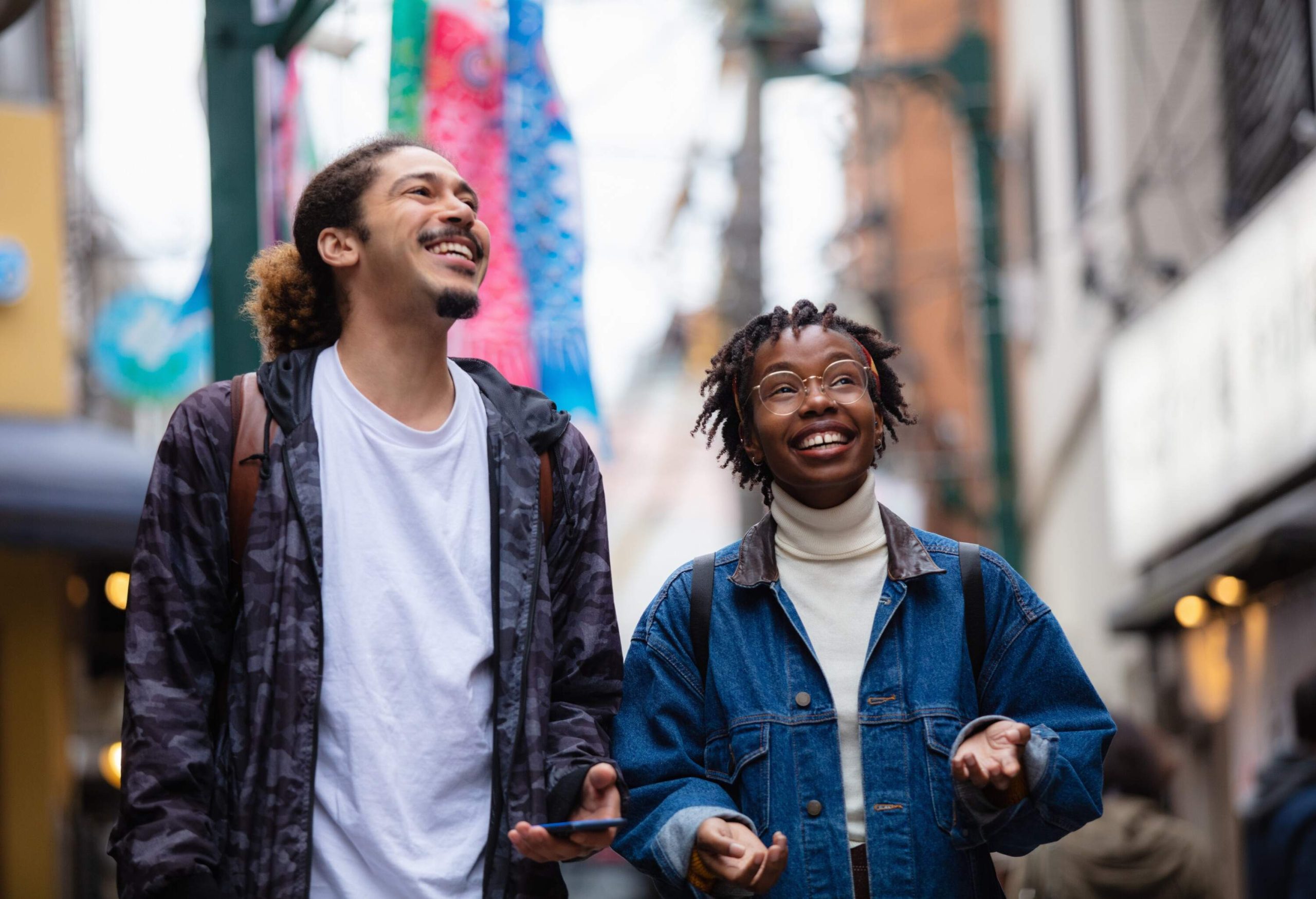 Two individuals laugh as they walk along the street.