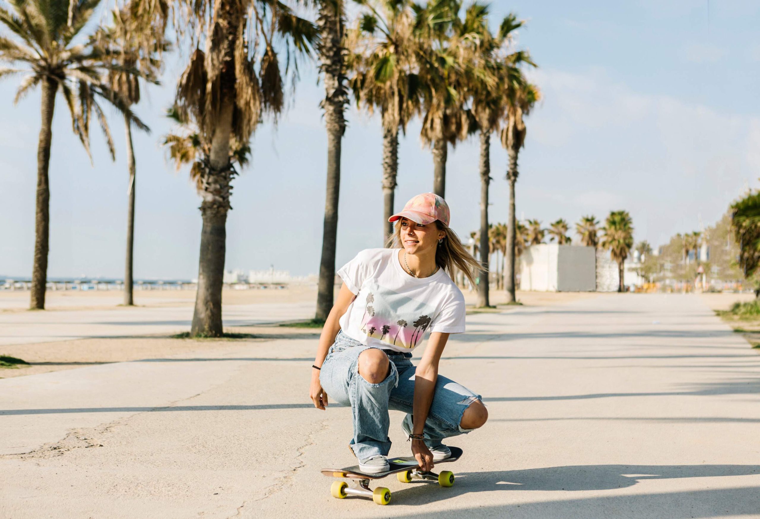 A female riding her skateboard on a paved road of the beach lined with tall trees.