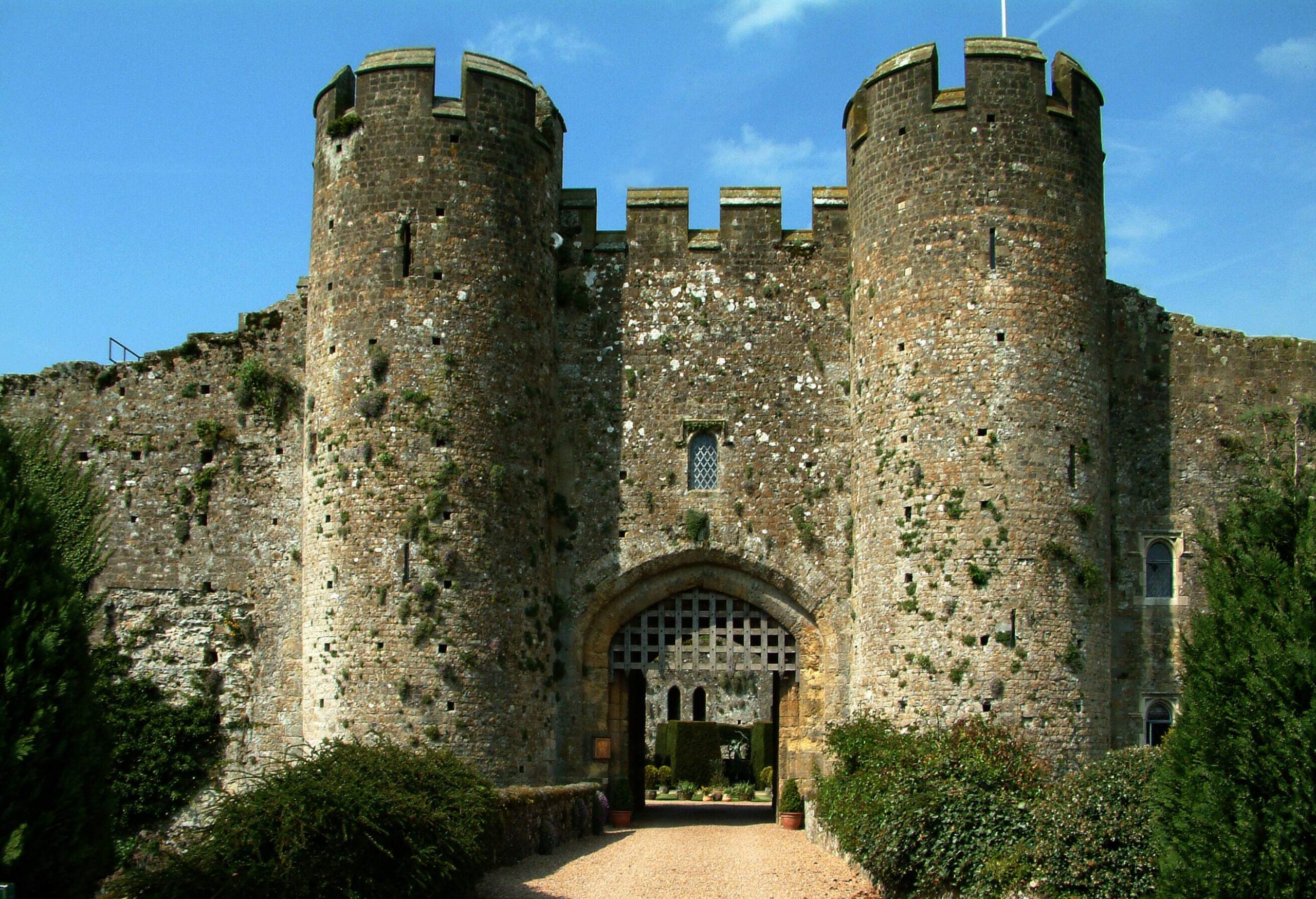 An entryway to an old castle with a portcullis and two towers on either side, all surrounded by bushes.