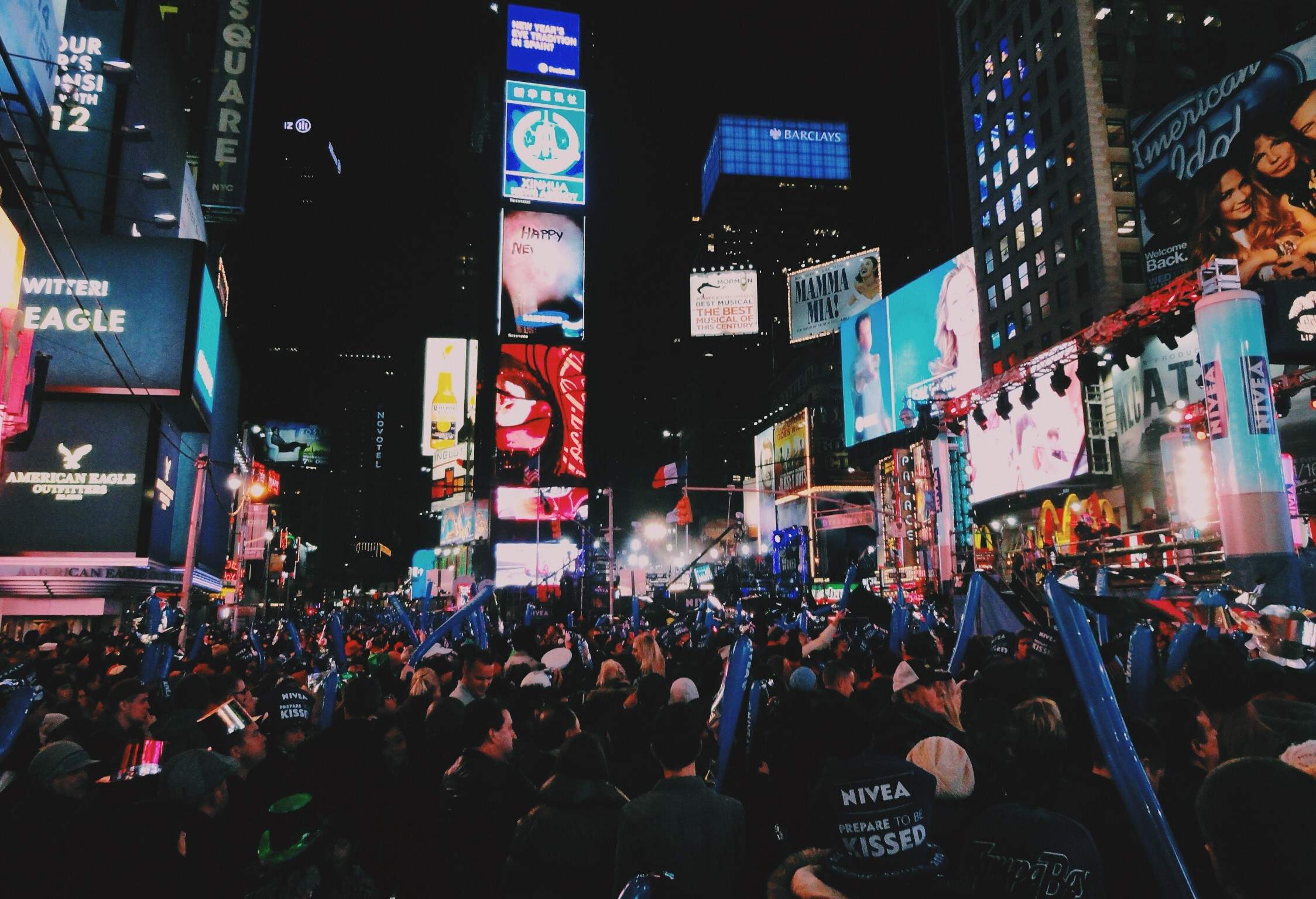 A night-time view of a crowded Times Square surrounded by buildings with bright billboards.
