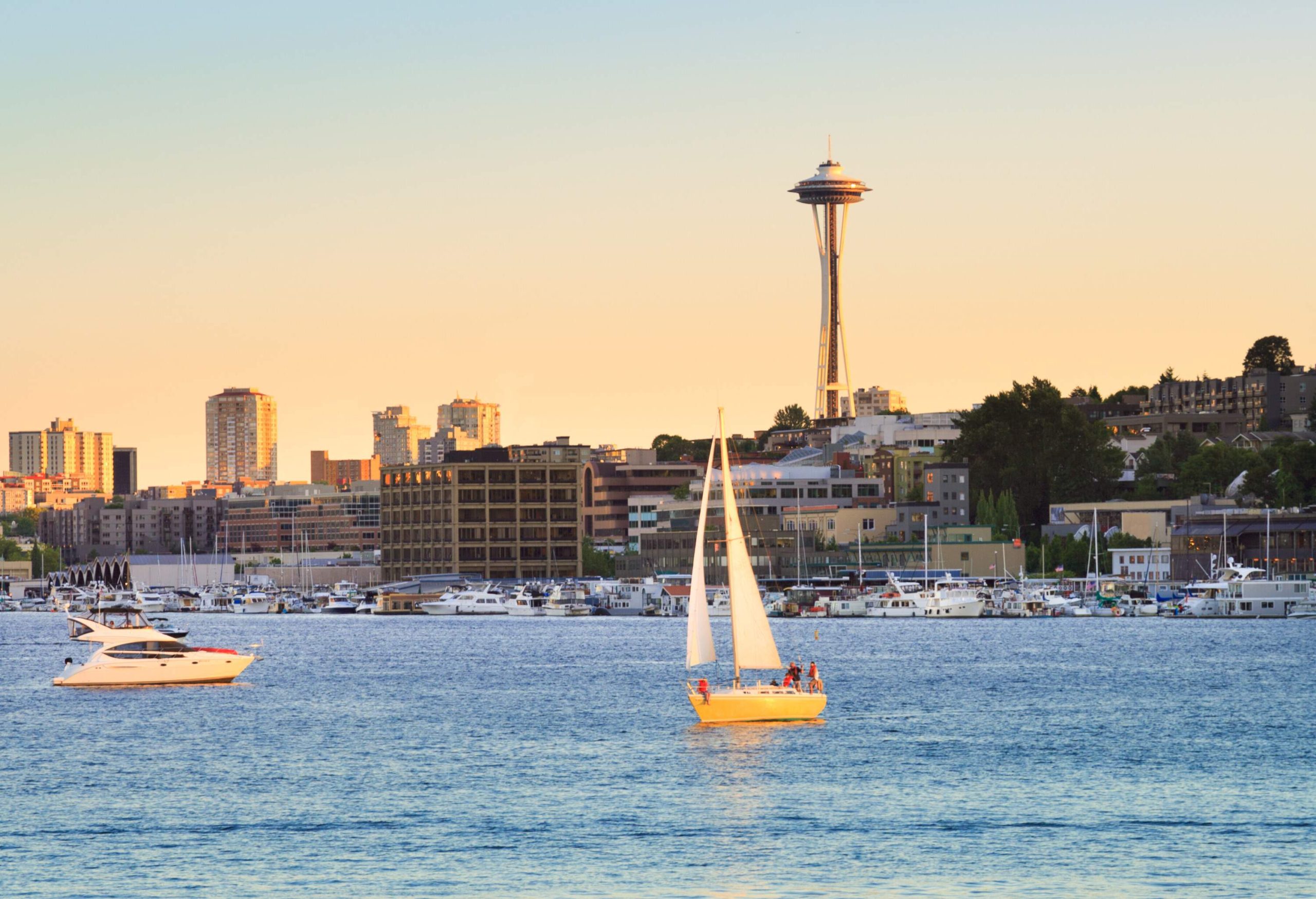 Boats gently float on the calm surface of a tranquil lake surrounded by a picturesque coastal town and a towering observation deck against the scenic twilight sky.
