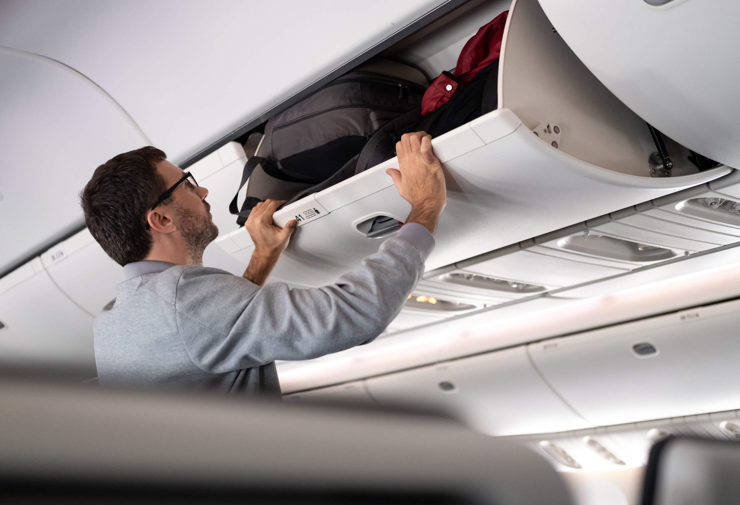 A man loading and securing his bags in the overhead compartment of the airplane.
