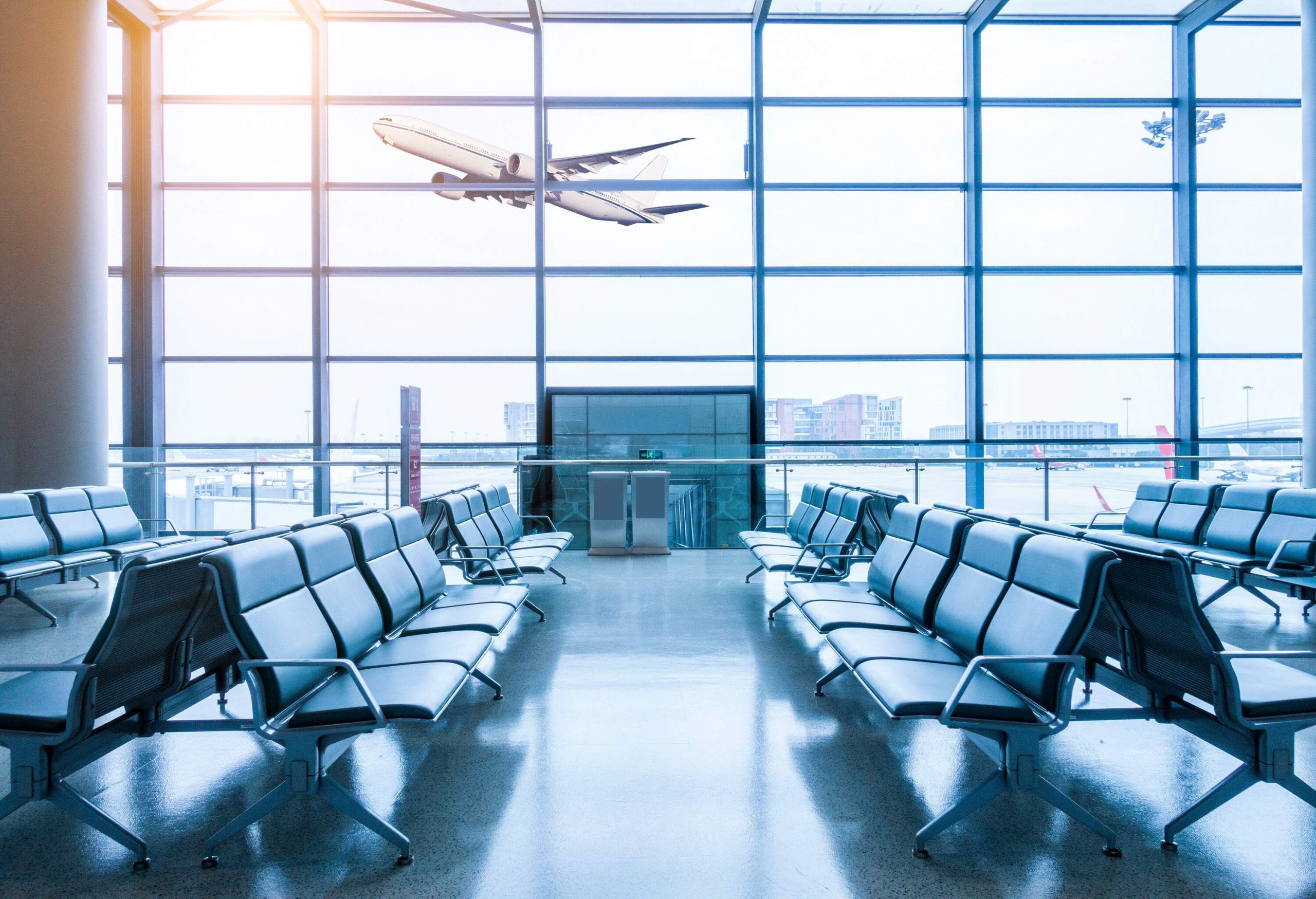 An airport terminal with empty seats and a glimpse of an airplane that just took off through the glass windows.