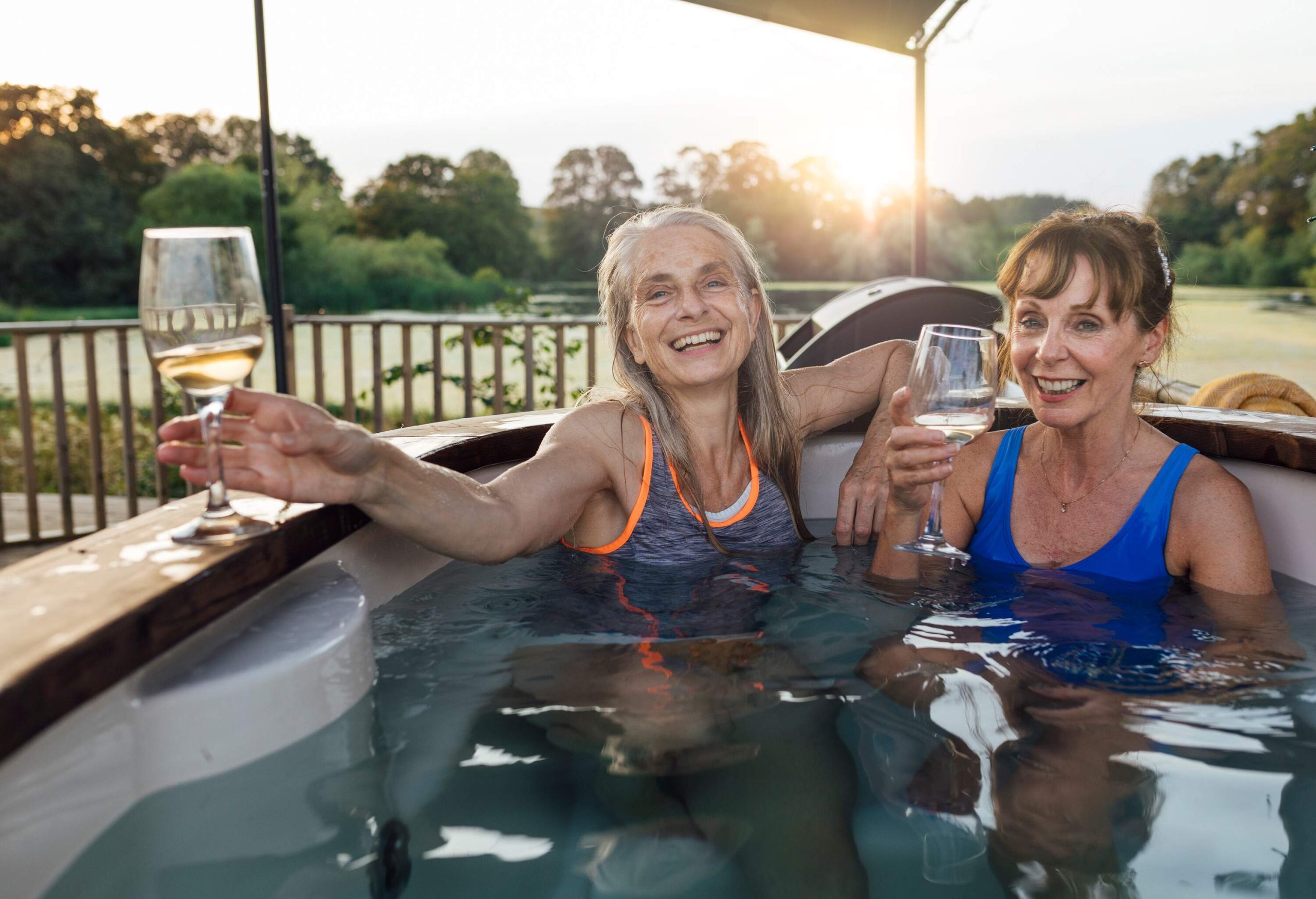Two mature women submerged in a hot tub while drinking wine.