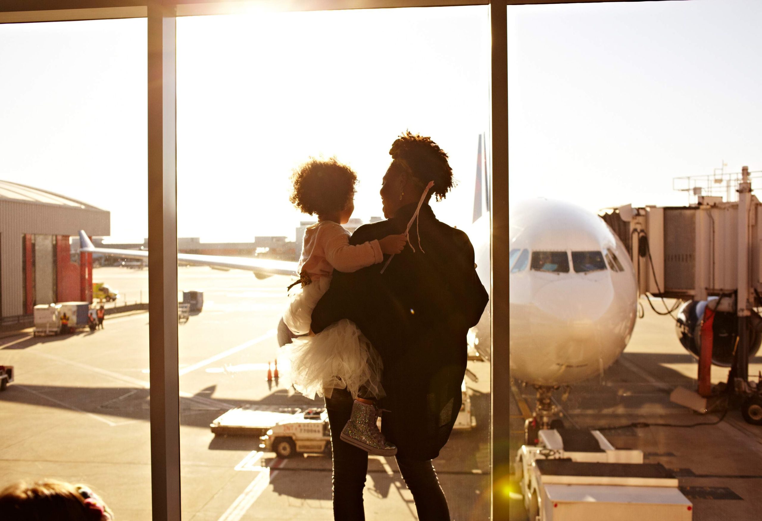 A mother holding her daughter as they look at an aircraft from the terminal.