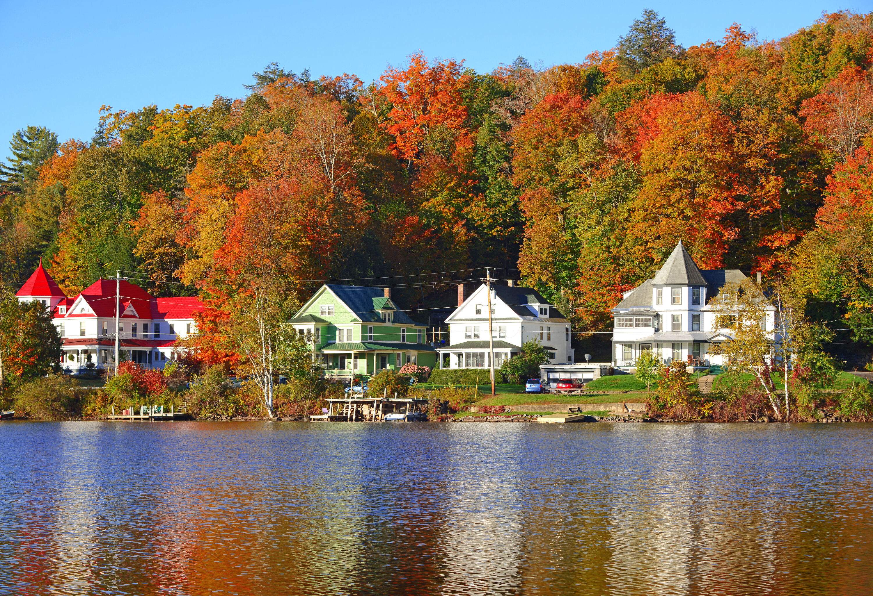 Charming Victorian houses along the shoreline of a lake shadowed by thick and tall trees in wonderful autumn hues.
