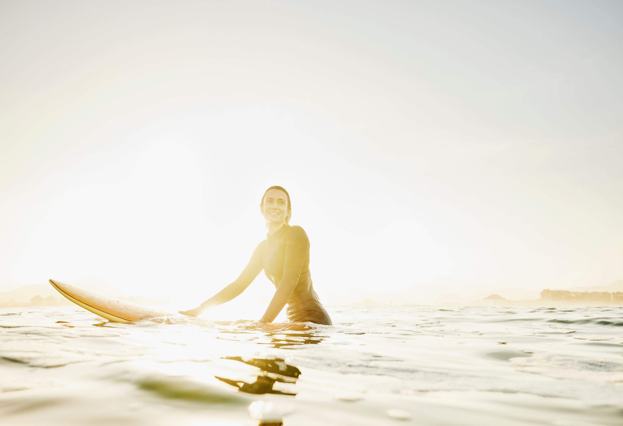 A woman sitting on her surfboard as it floats in the sea.