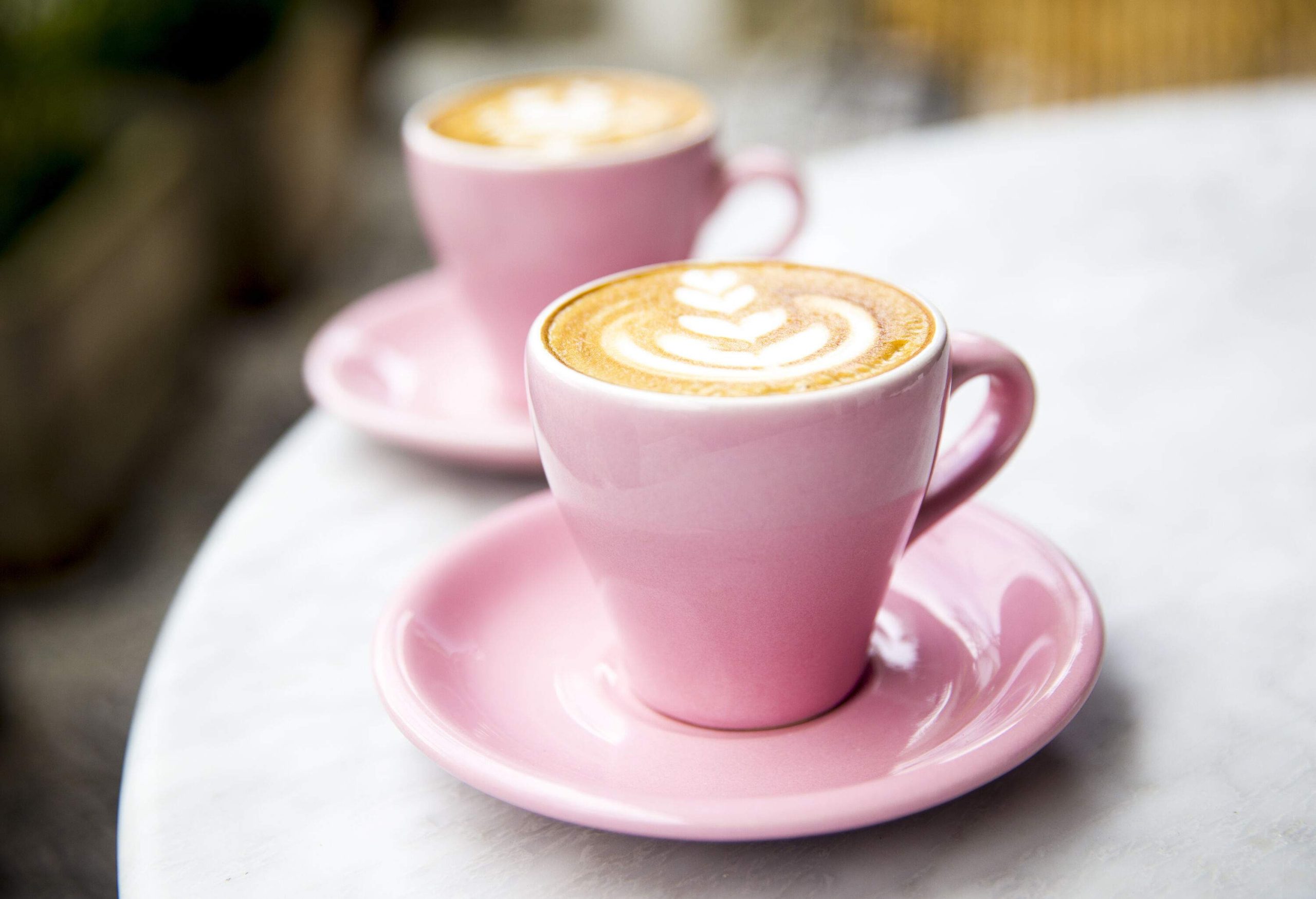Two pink cups of coffee with a leaf-shaped design were placed on a table.