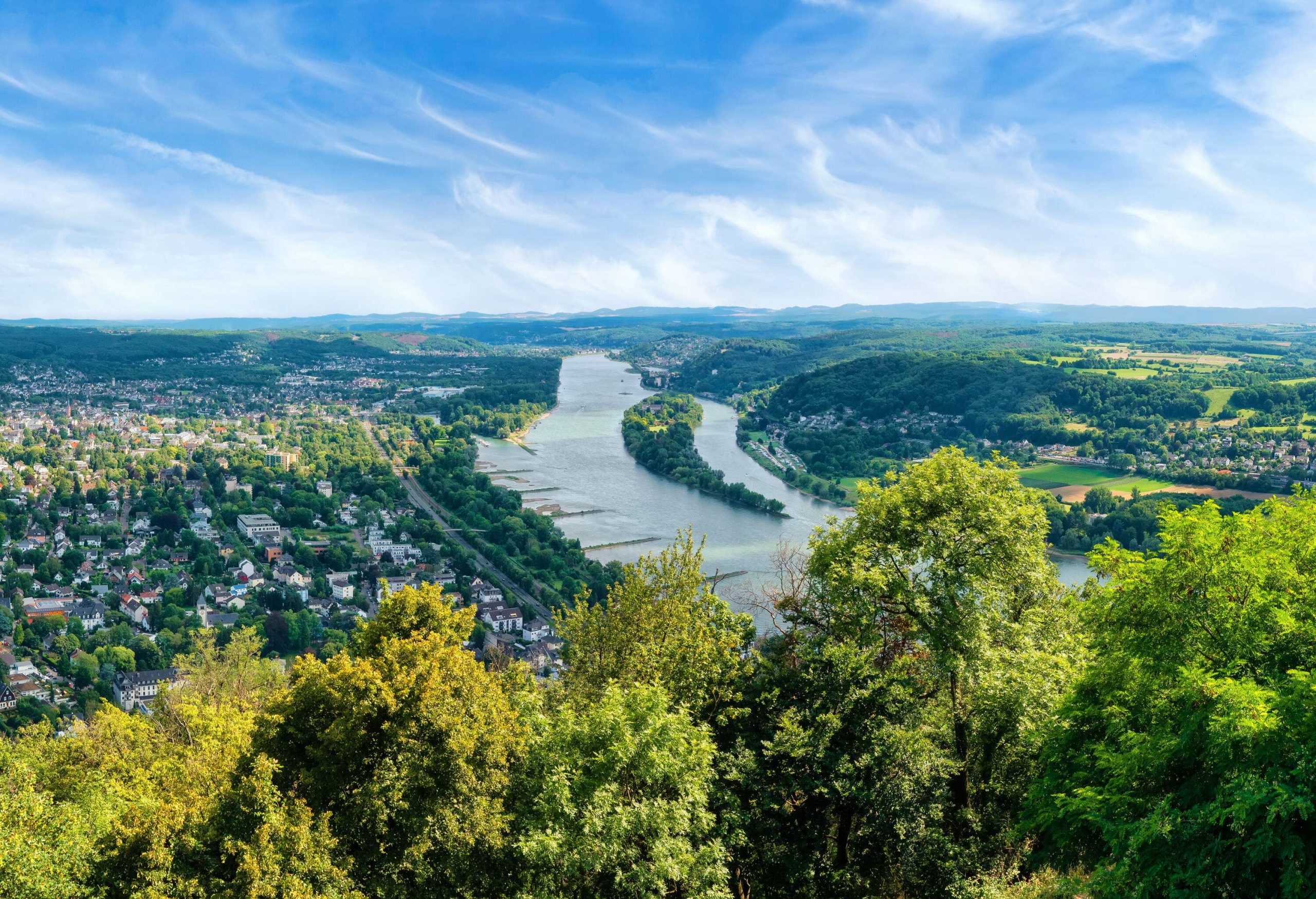 A broad river flows in the middle of a vast lush land with scattered houses and trees.