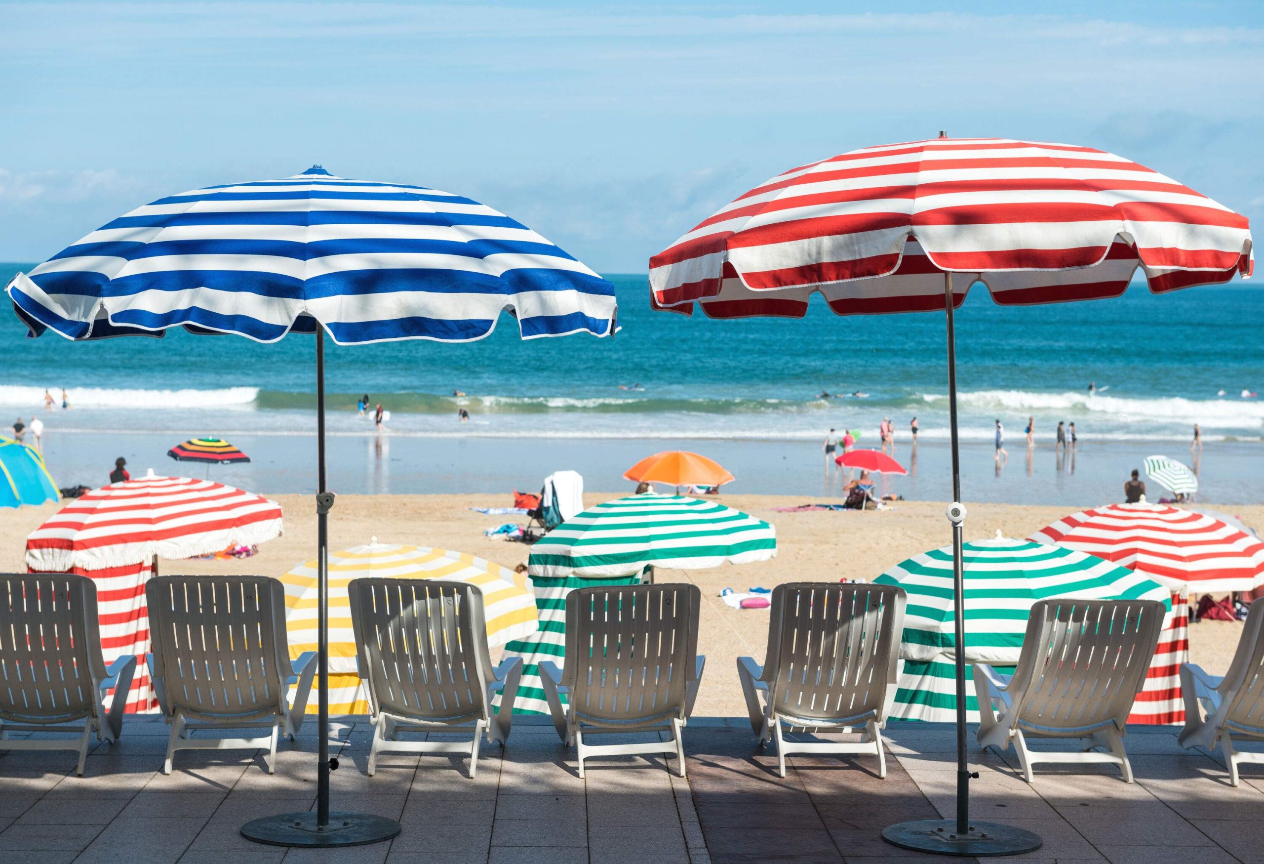 White sun loungers under colourful striped umbrellas facing out into the sea.