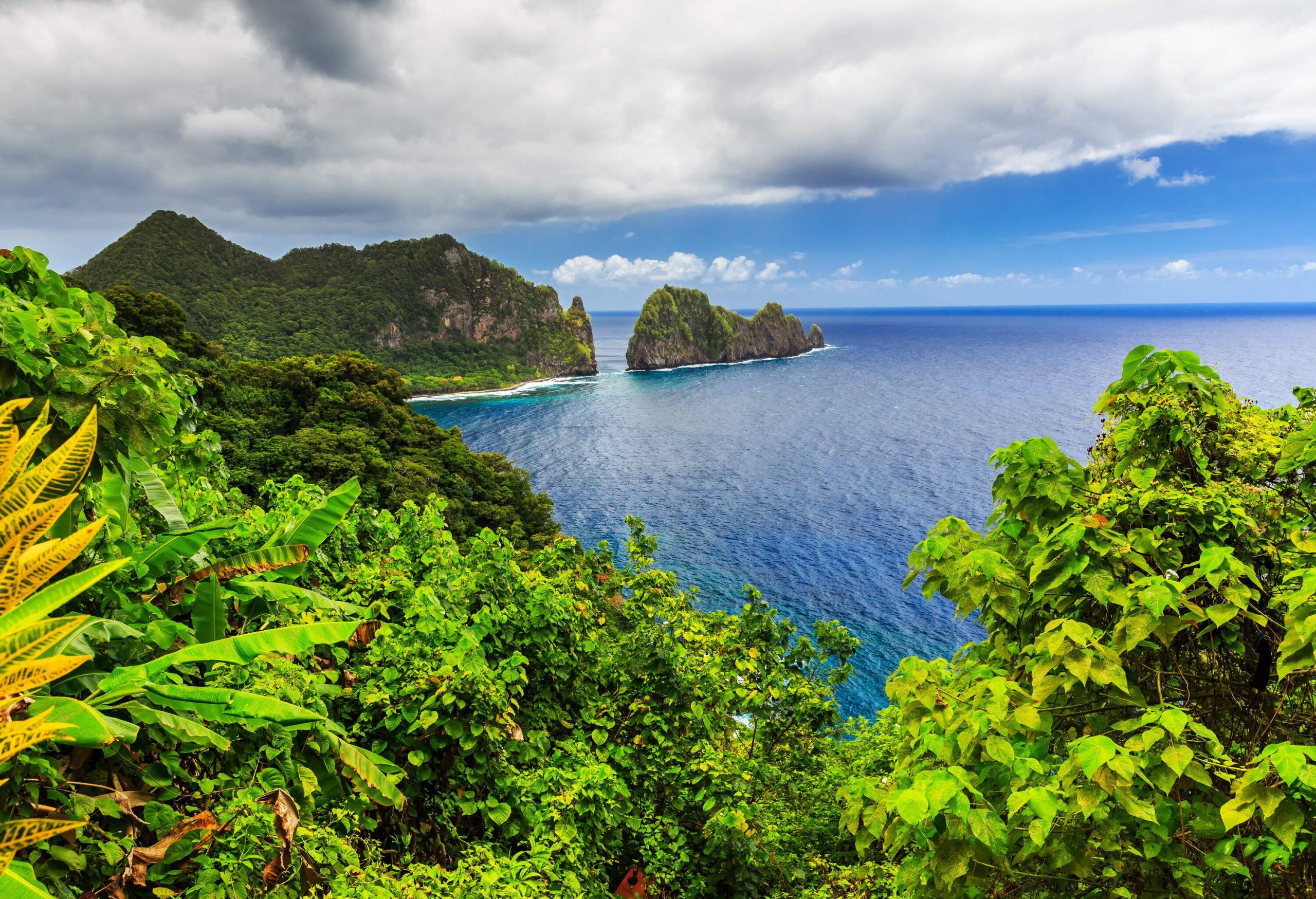 A verdant rocky island surrounded by the blue sea against the cloudy blue sky.