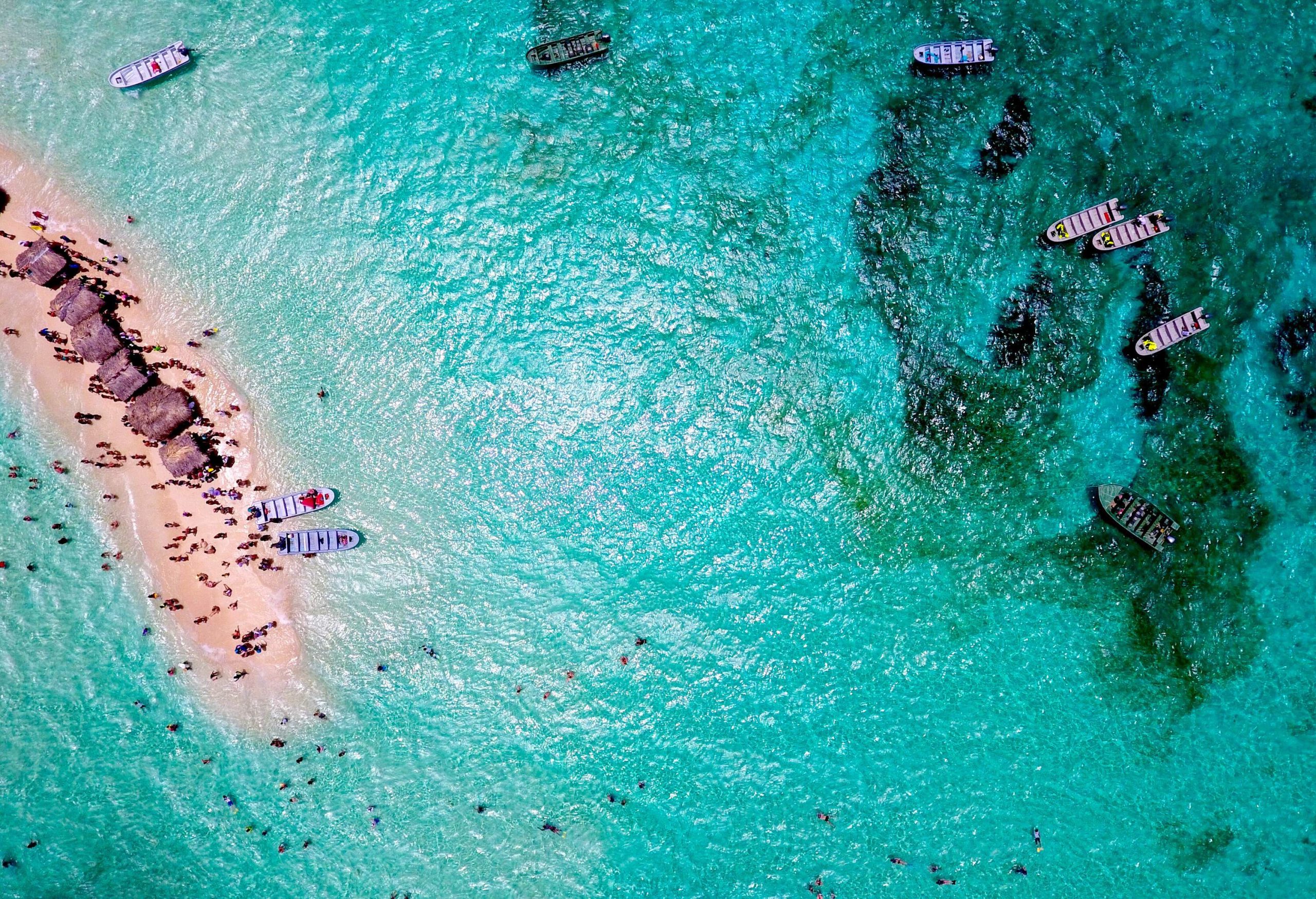 A narrow sandbank surrounded by turquoise seas, populated by beach cottages and people enjoying the nice weather.