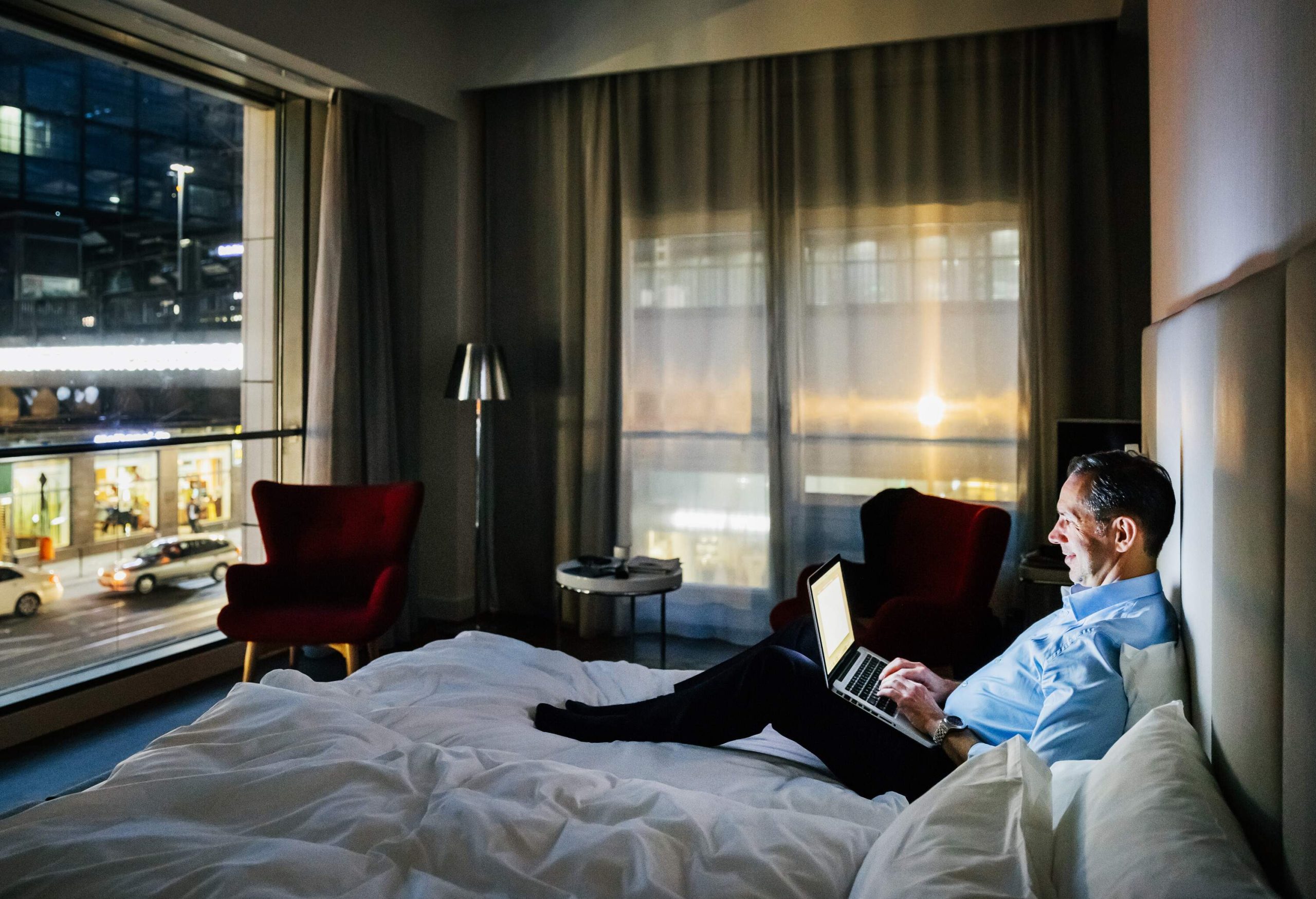 Businessman sat on hotel bed, working from his laptop.