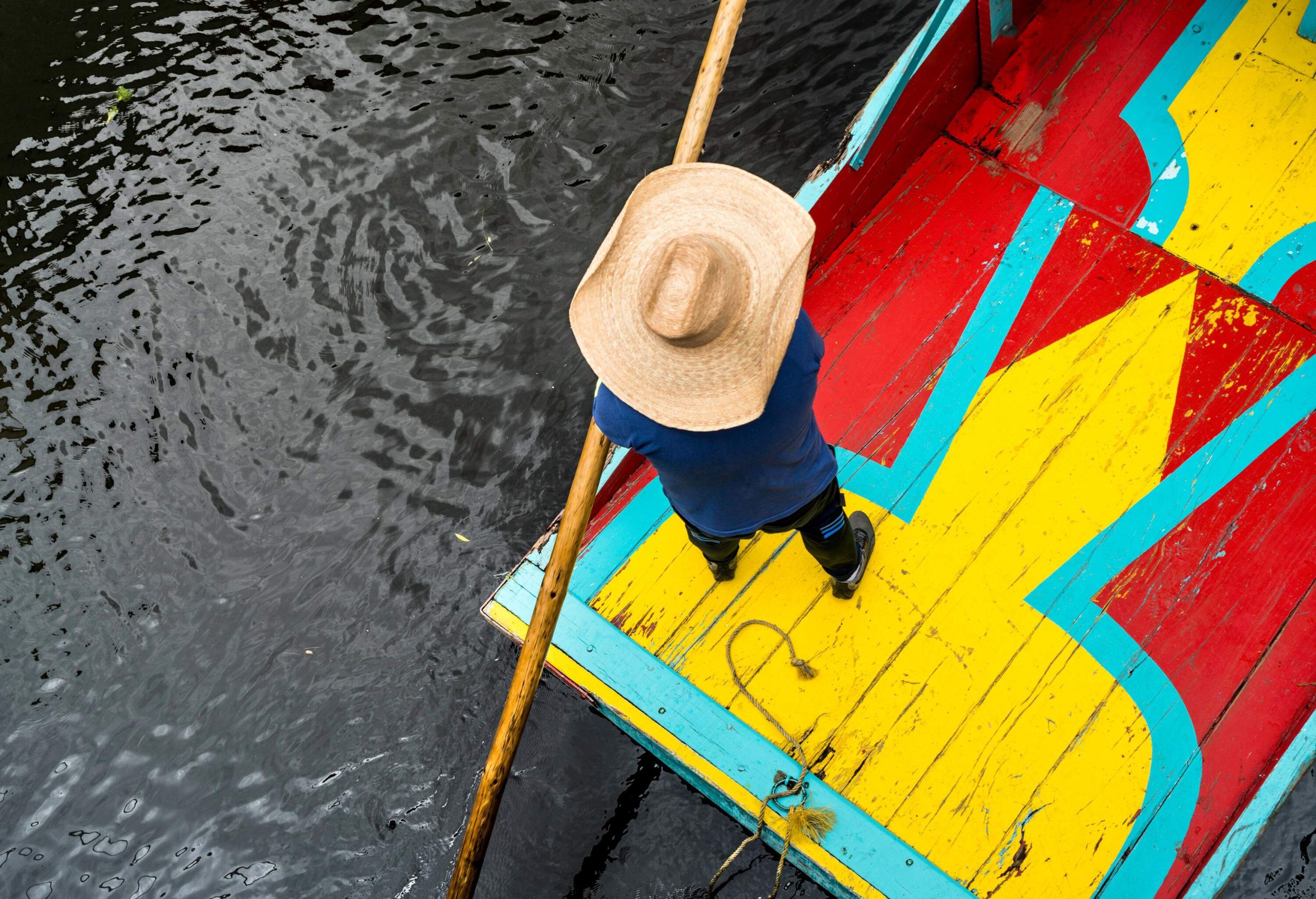 Top view of an individual standing on a colourful boat over a canal.
