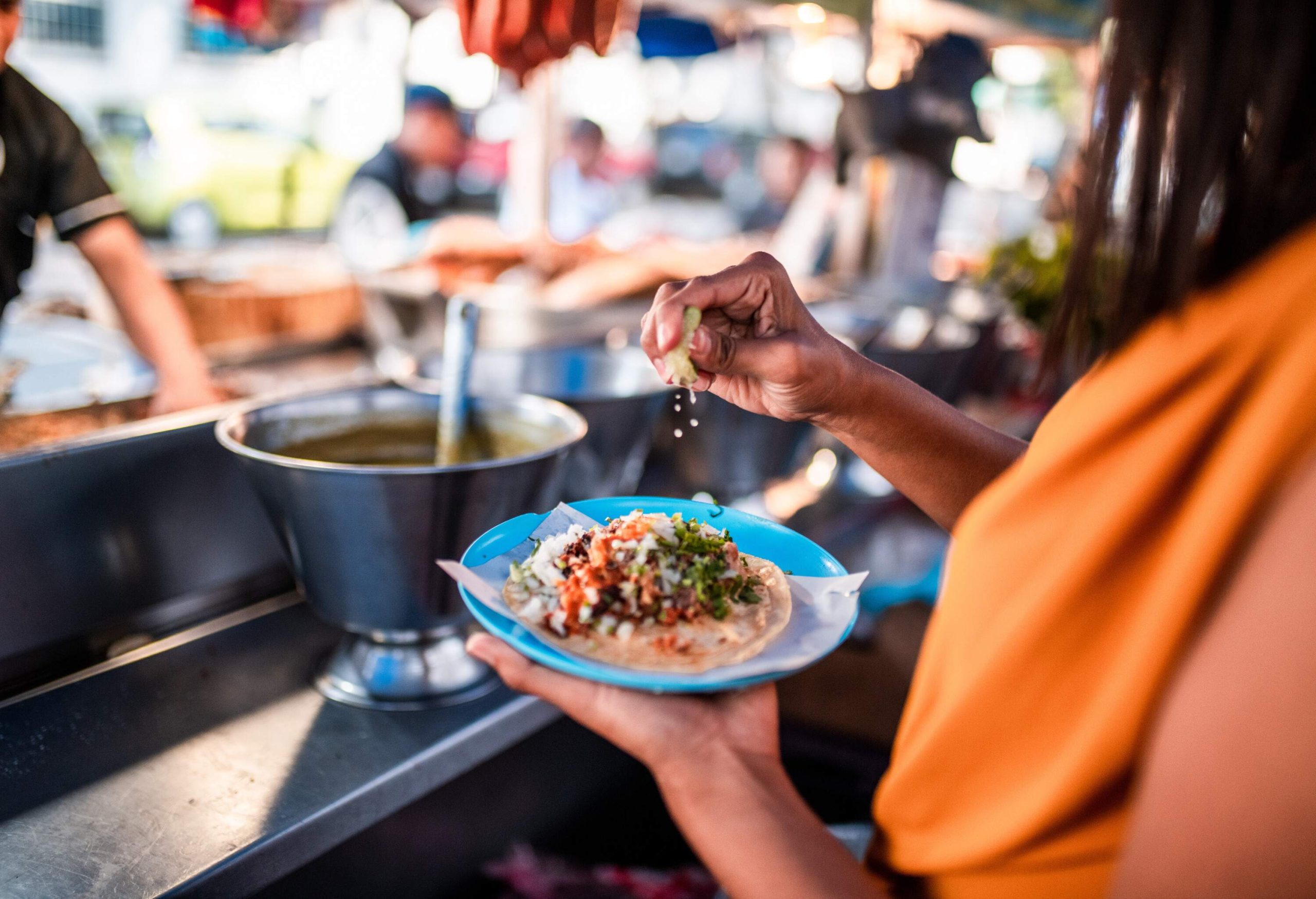 A person squeezes a lemon slice into a platter of tacos while holding it.