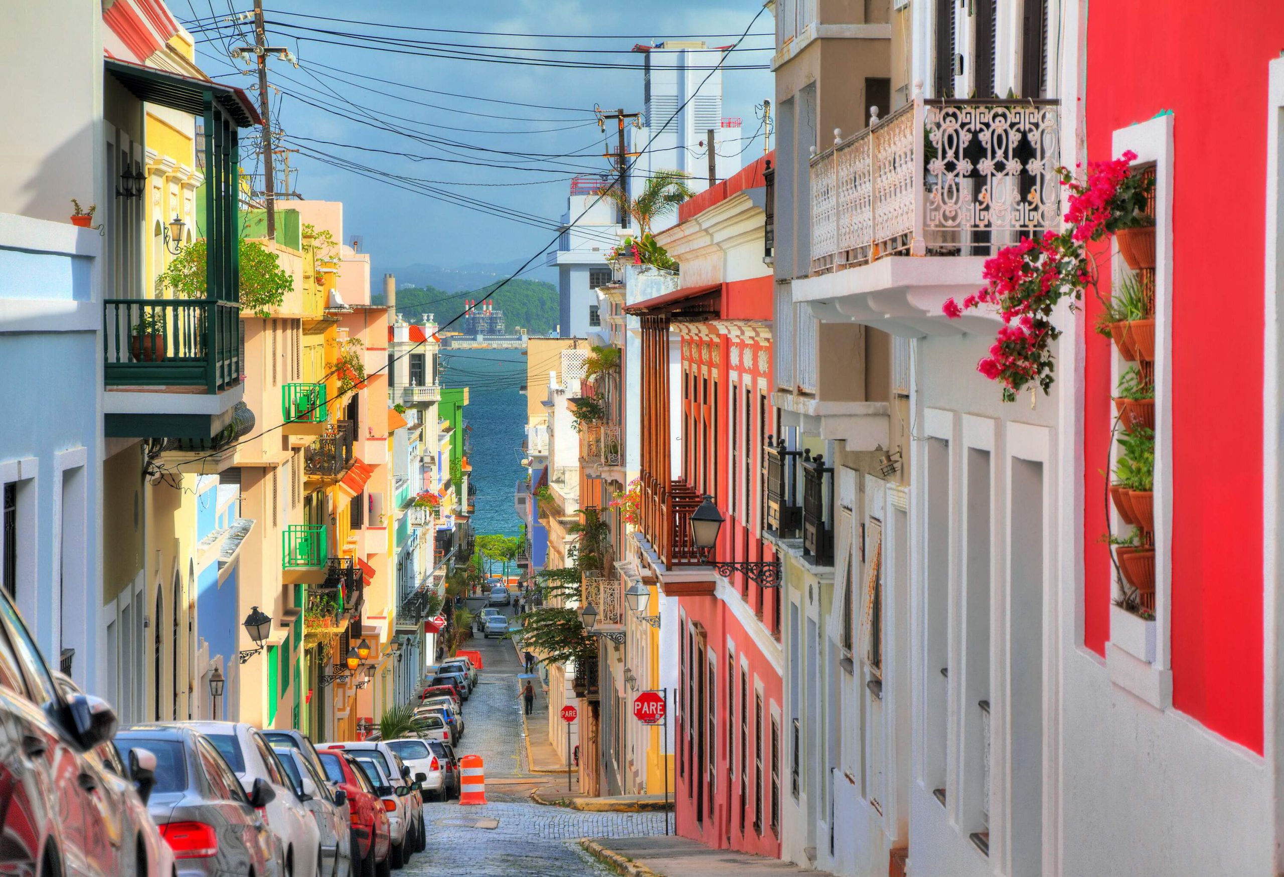 A narrow street with parked vehicles on one side flanked by colourful buildings.