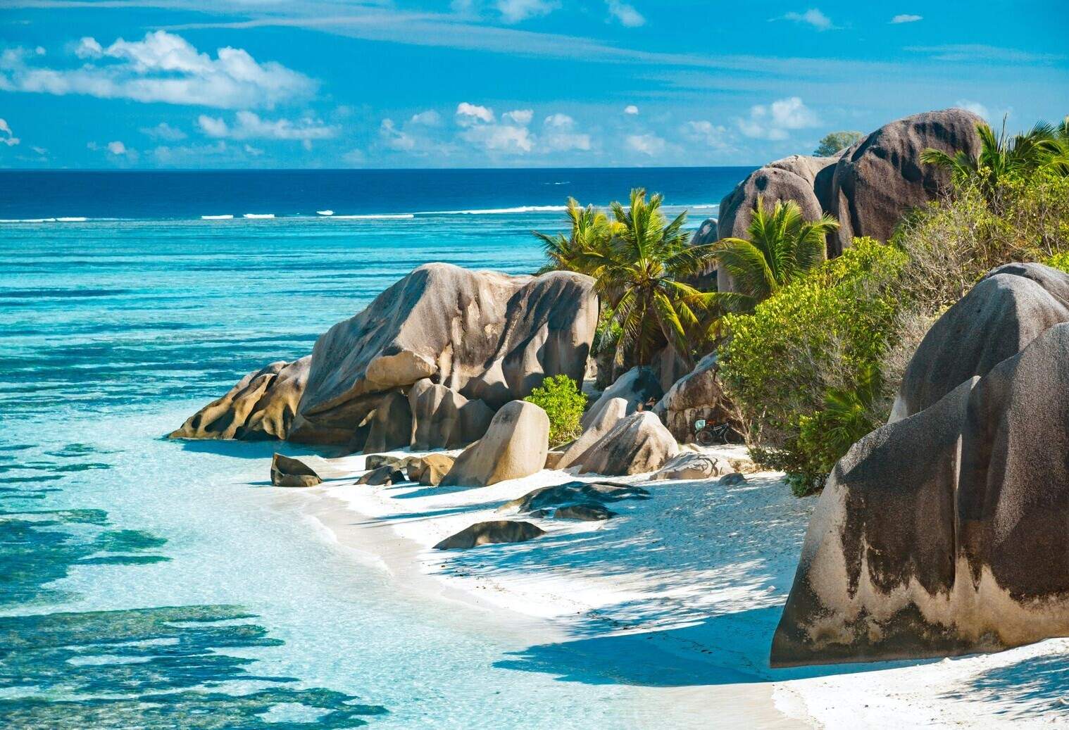 A scenic landscape of rocks emerges on the coast between the lush trees surrounded by turquoise seawater.