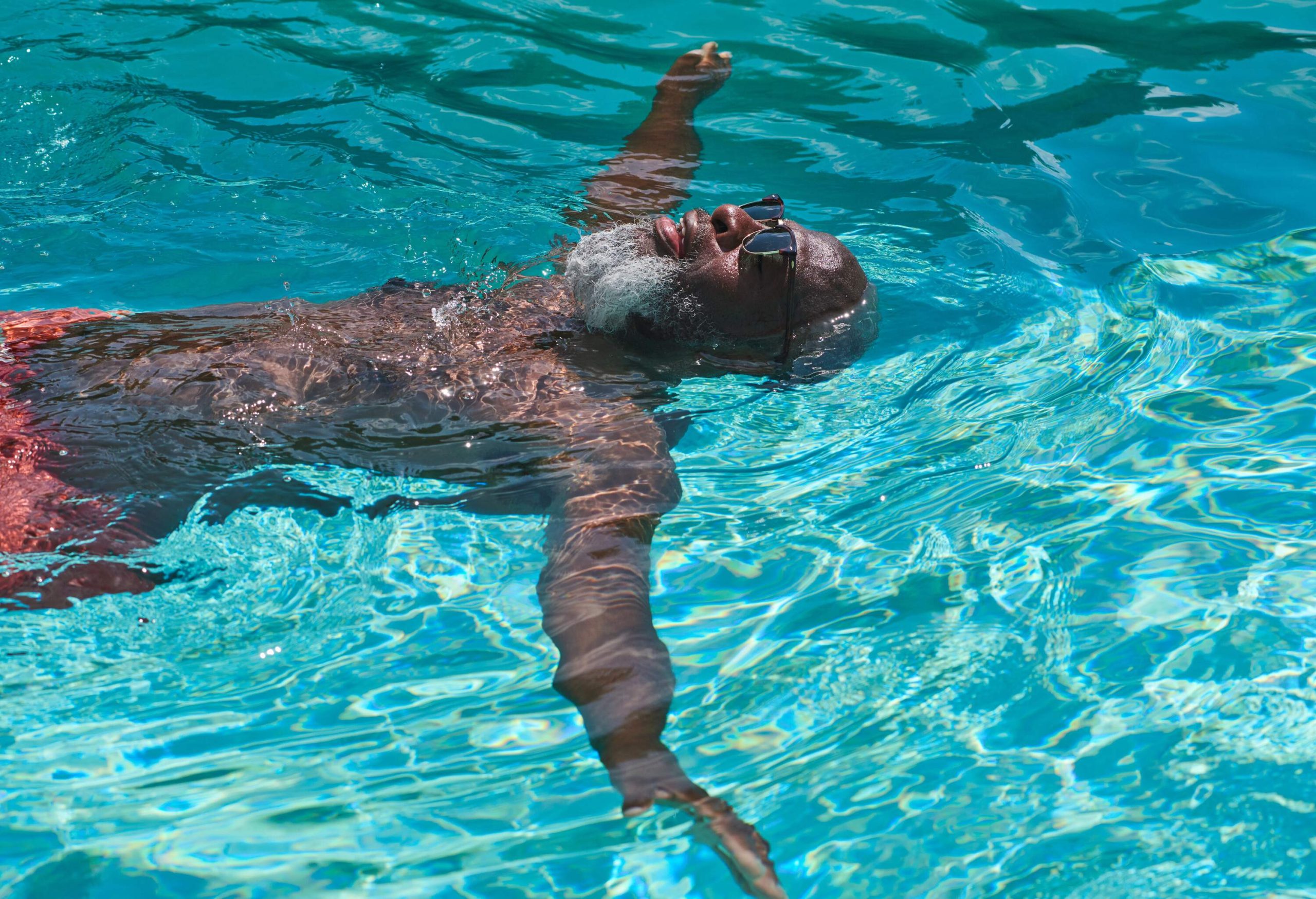 A mature man floats on his back, relaxing in his pool.