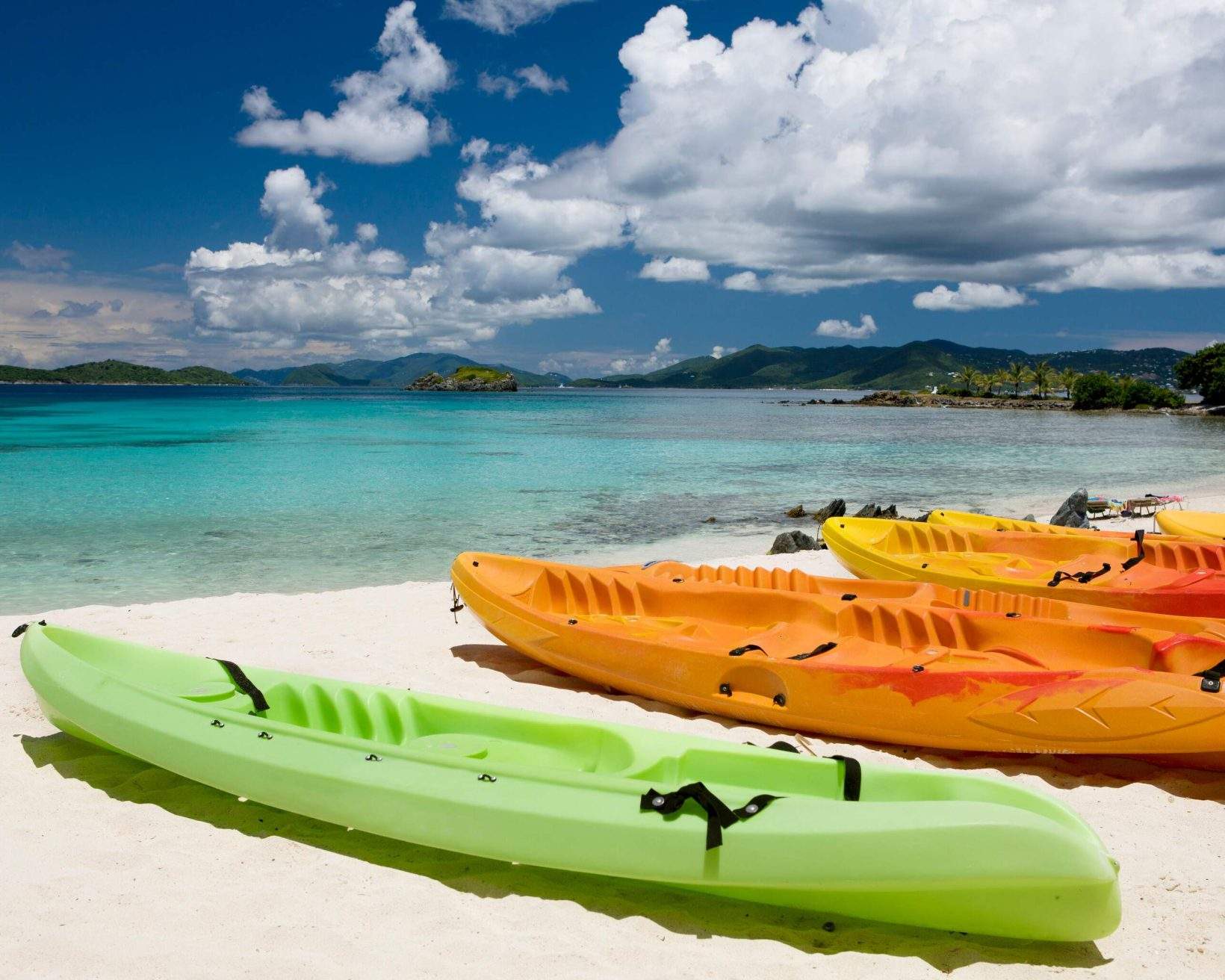 A row of colourful kayaks parked on a white beach.