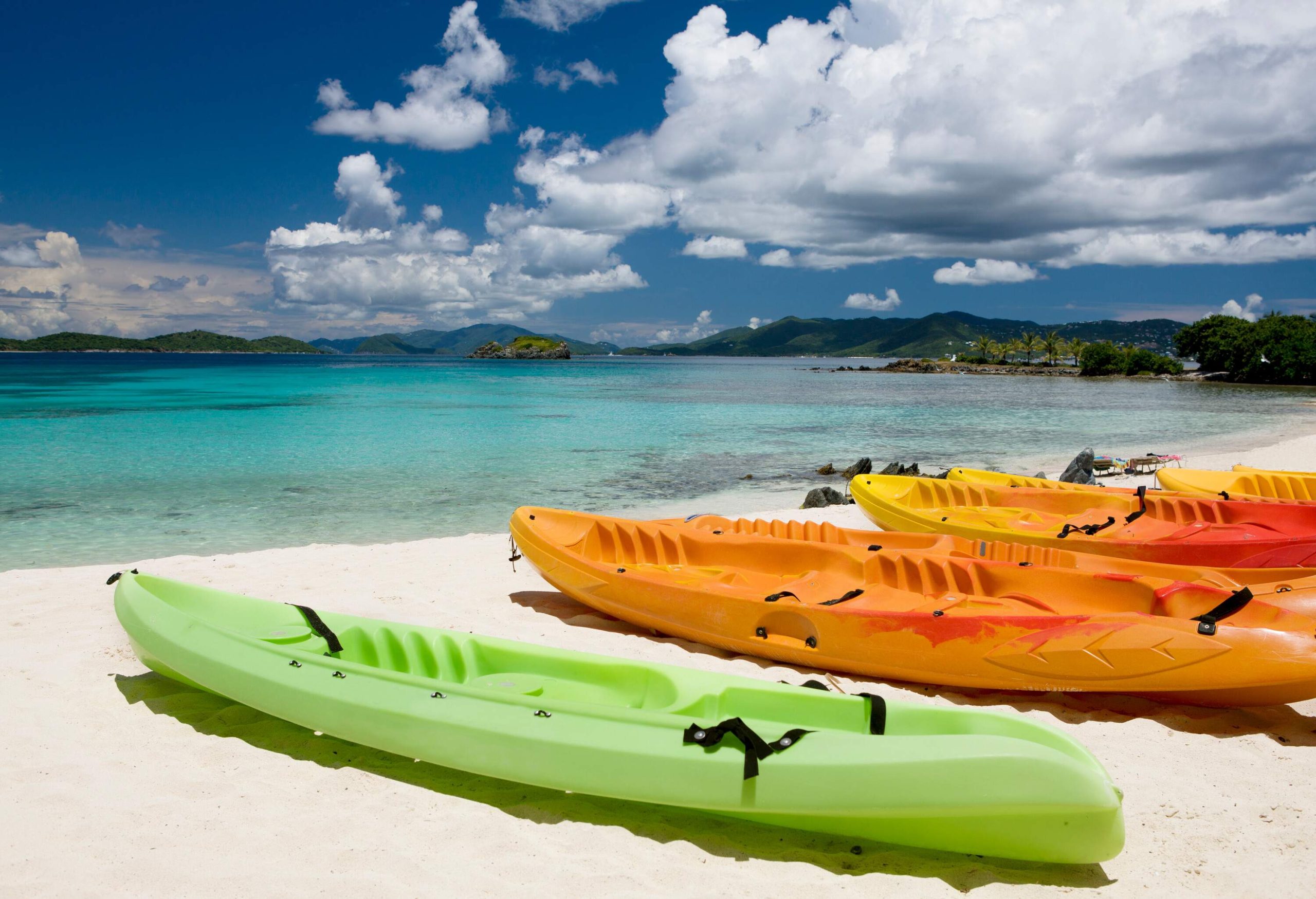 A row of colourful kayaks parked on a white beach.