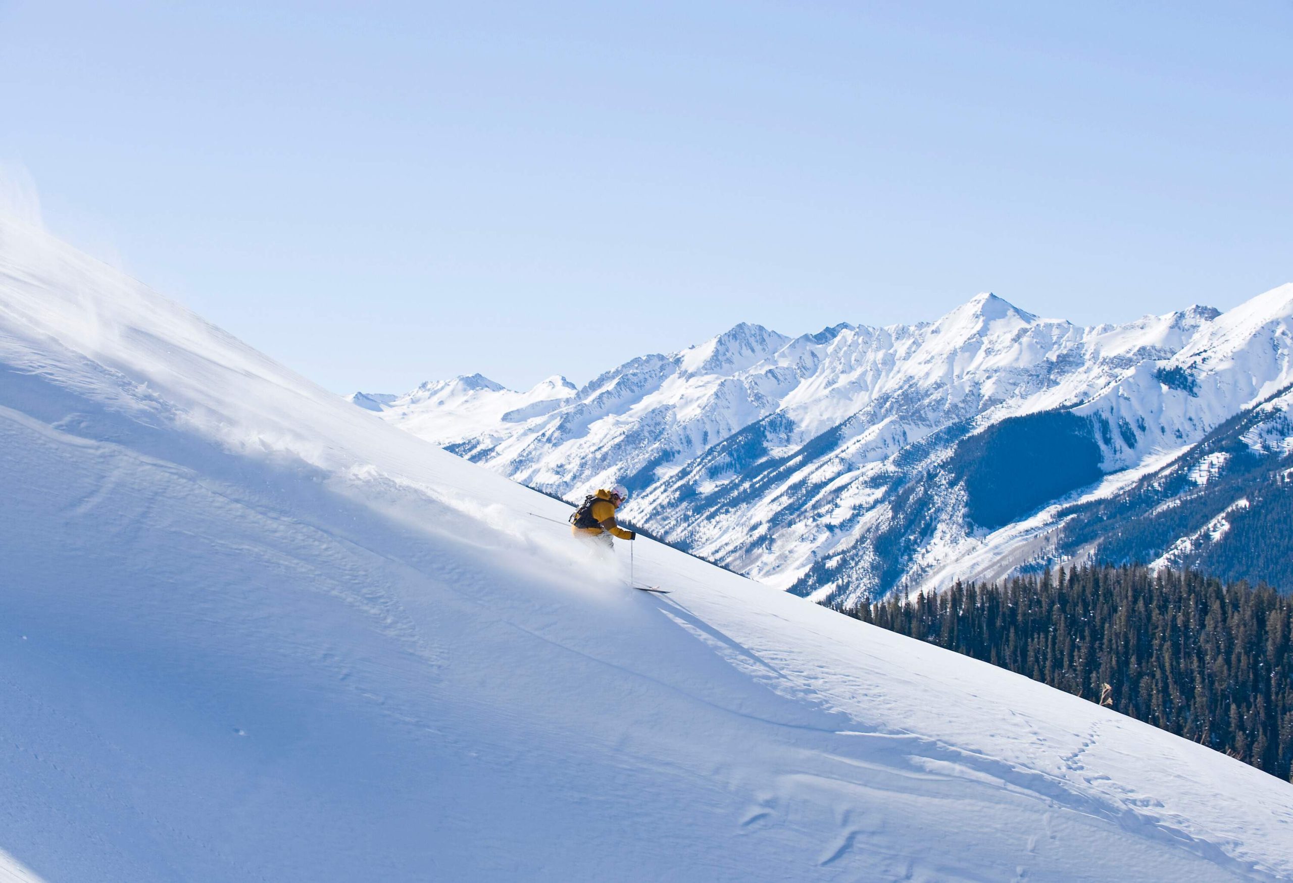 A skier sliding down a big mountain run with mountains and a forested valley in the distance.
