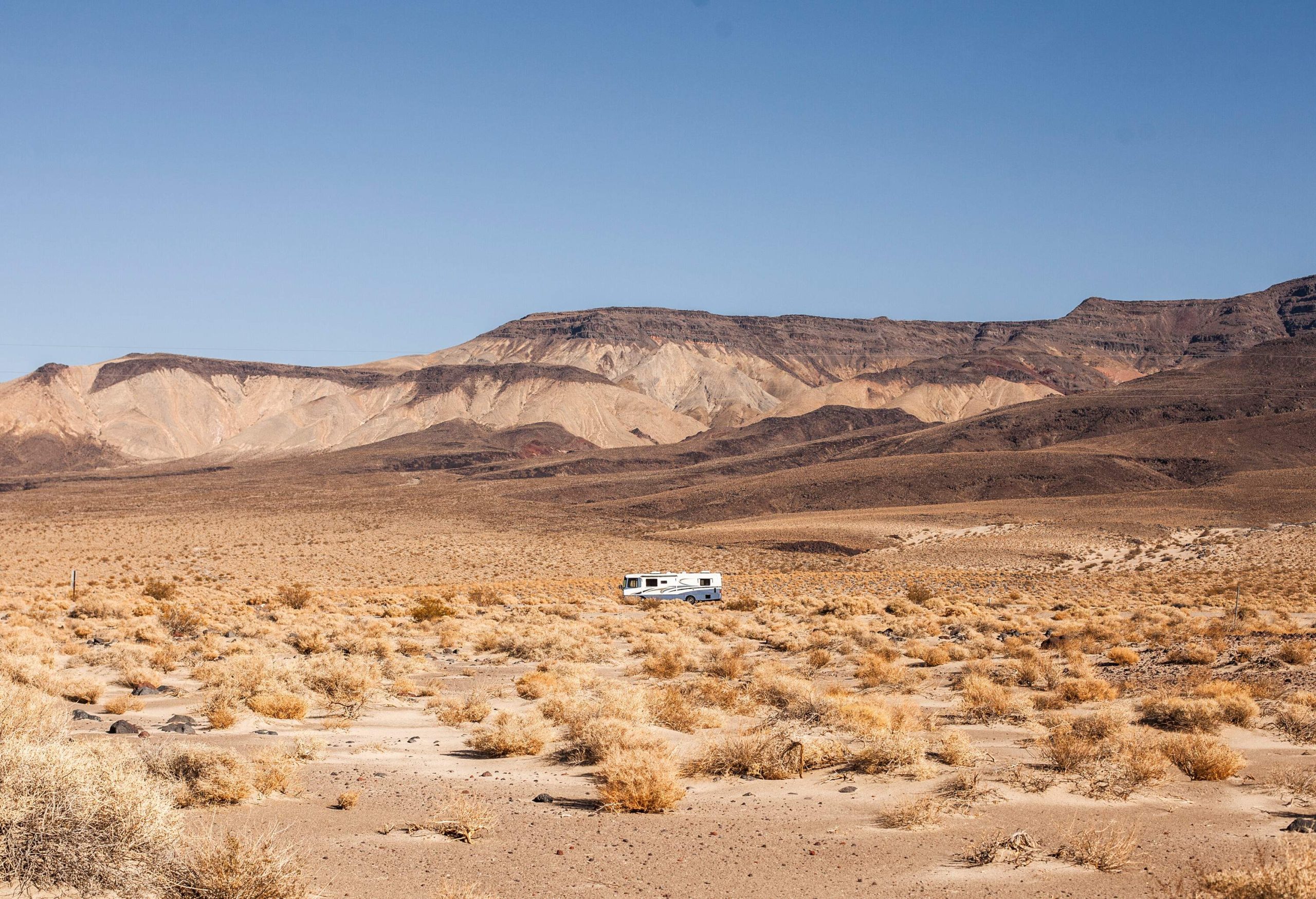 A camper van travelling across a desert with distant views of mountains.