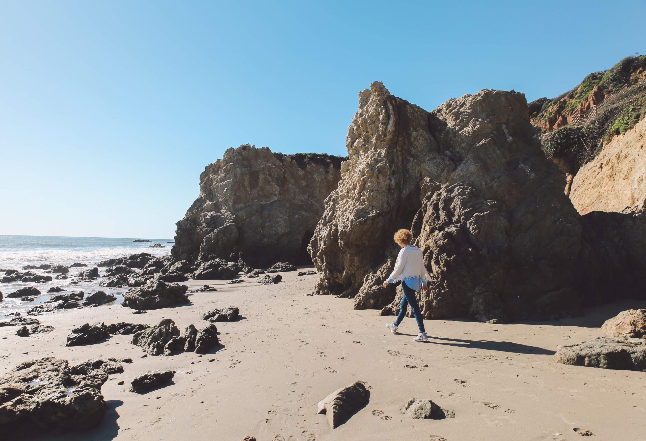 A woman dressed in casual attire gracefully stands on the shore of a rocky beach, embracing the beauty of nature's rugged landscape.