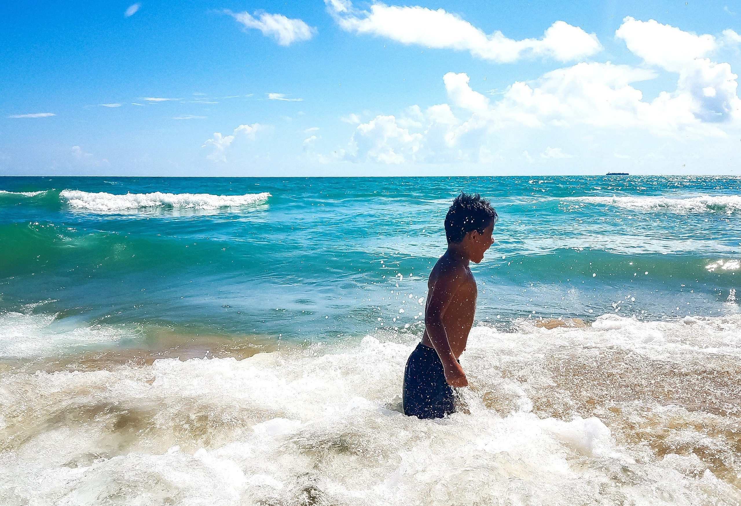 A young child stands on the shore as waves crash around them.
