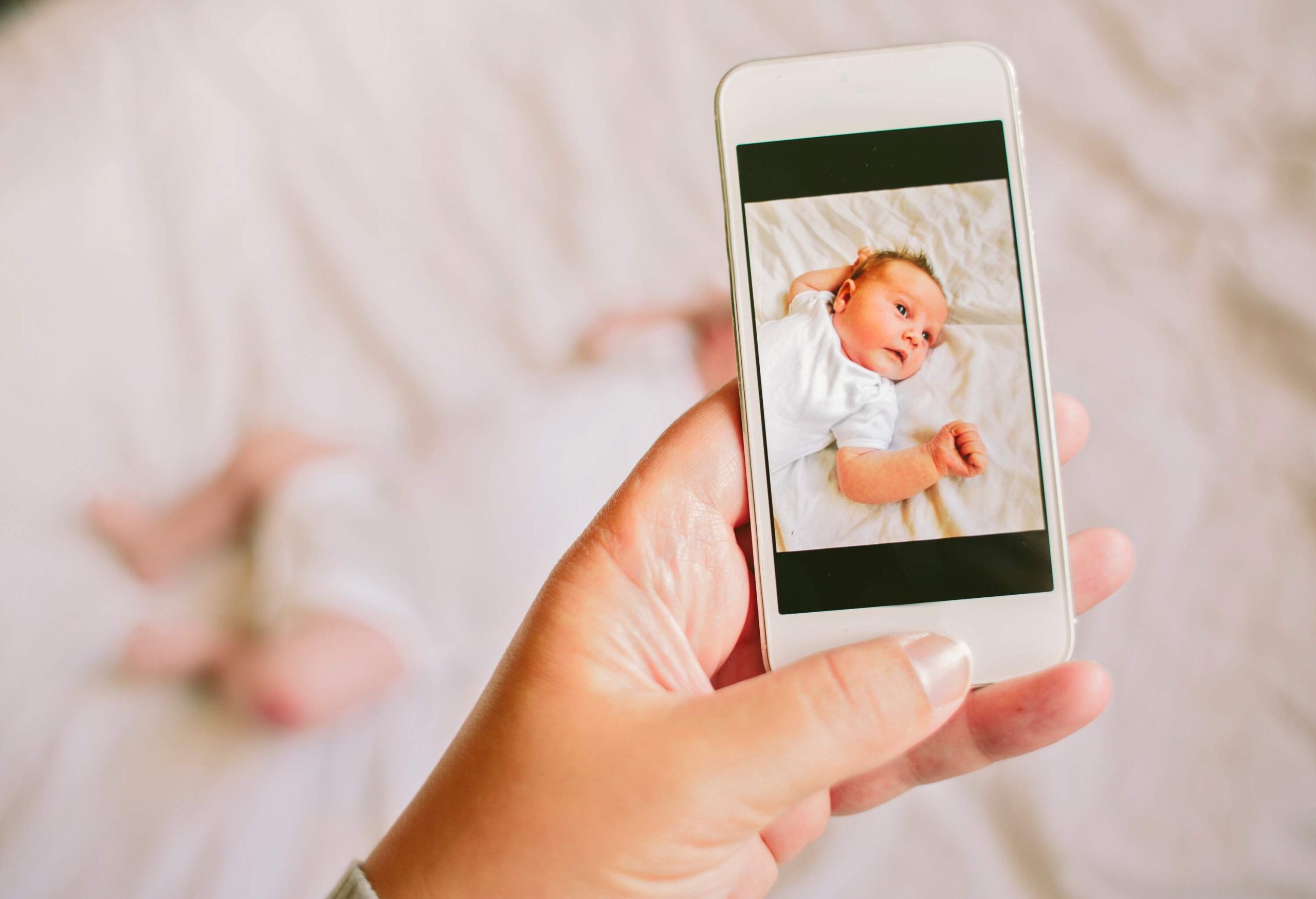 Mother taking a photograph on a smartphone of her newborn baby daughter