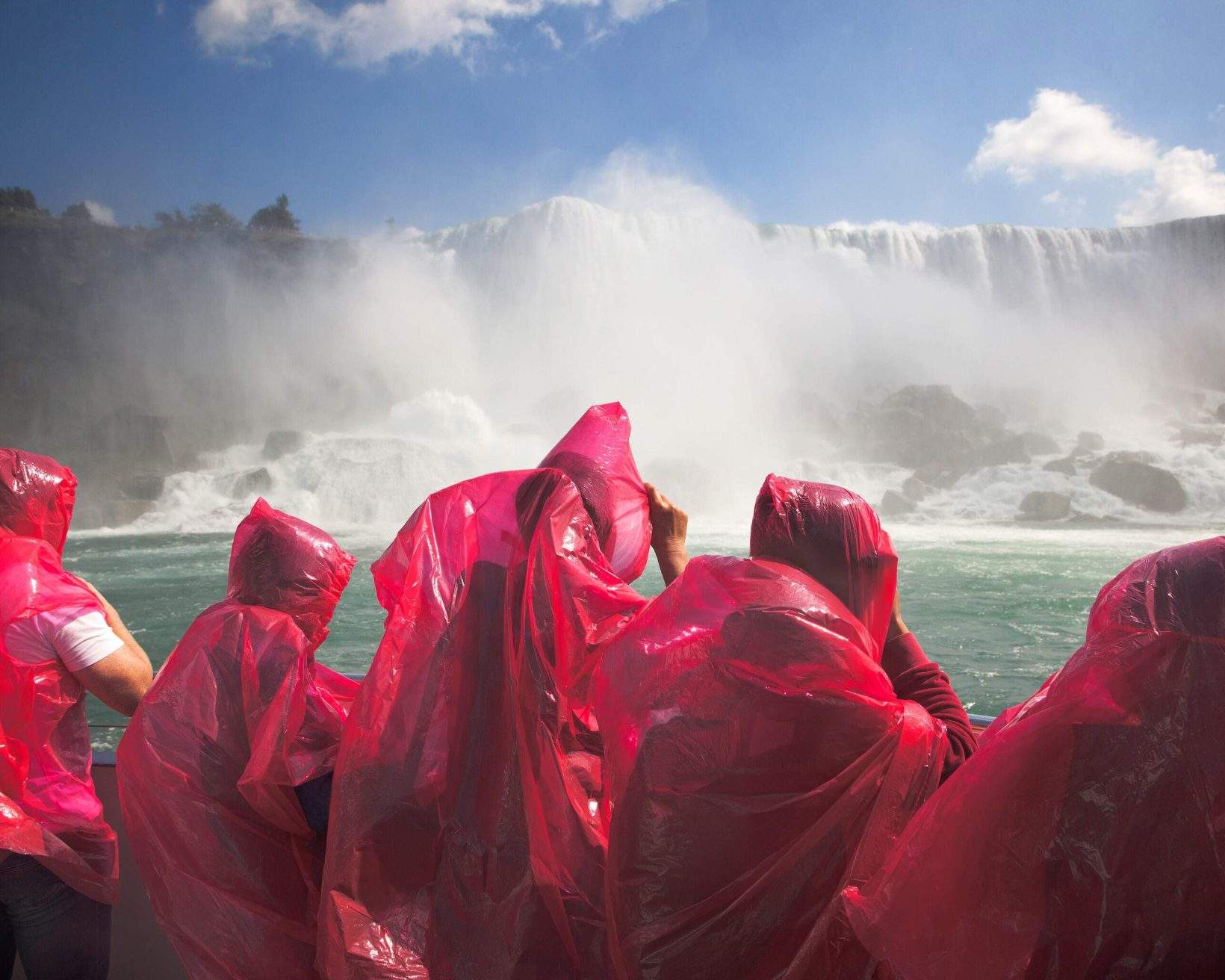 A group of individuals, clad in vibrant red plastic attire, enthusiastically gather around the majestic Niagara Falls.