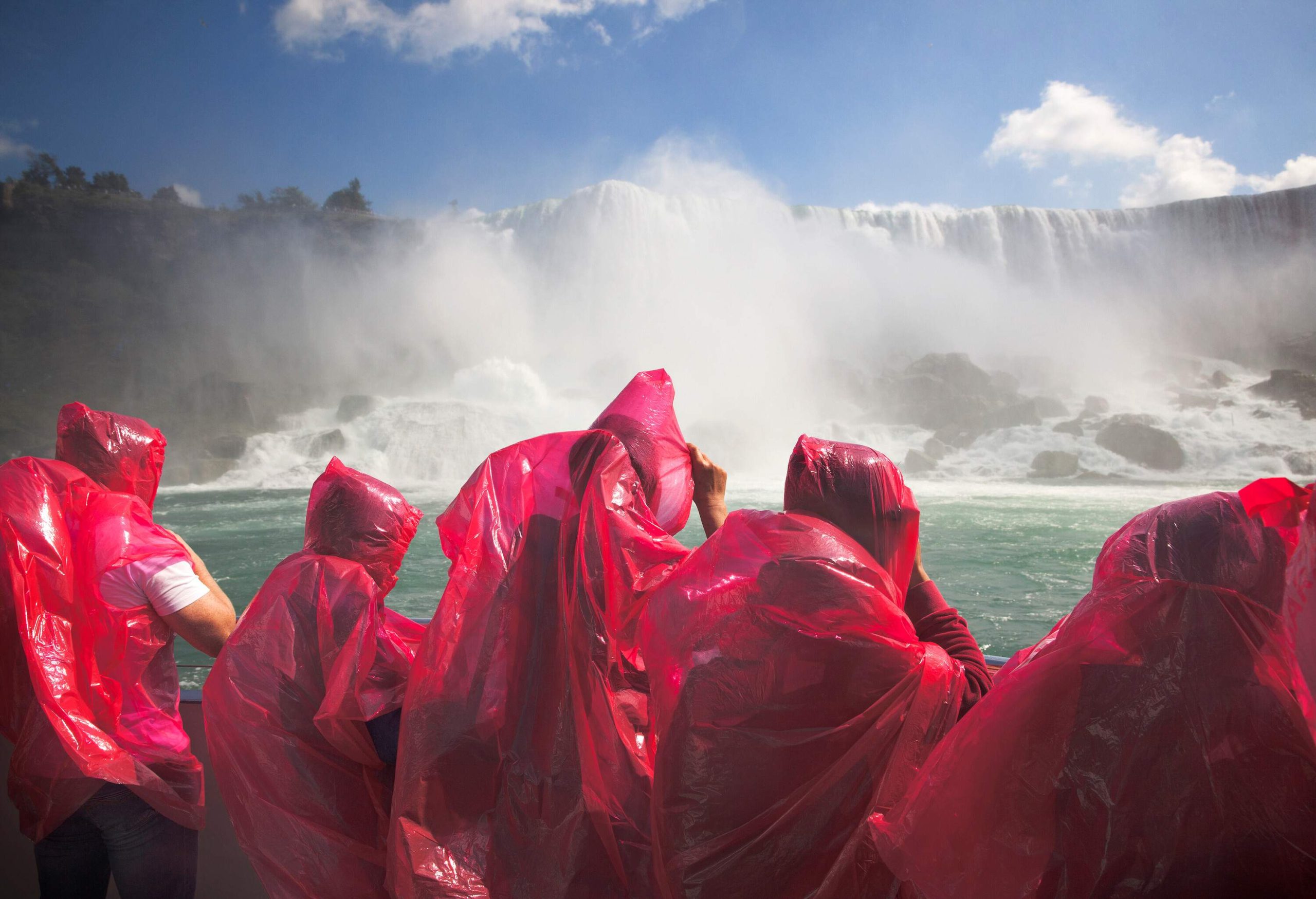 A group of individuals, clad in vibrant red plastic attire, enthusiastically gather around the majestic Niagara Falls.