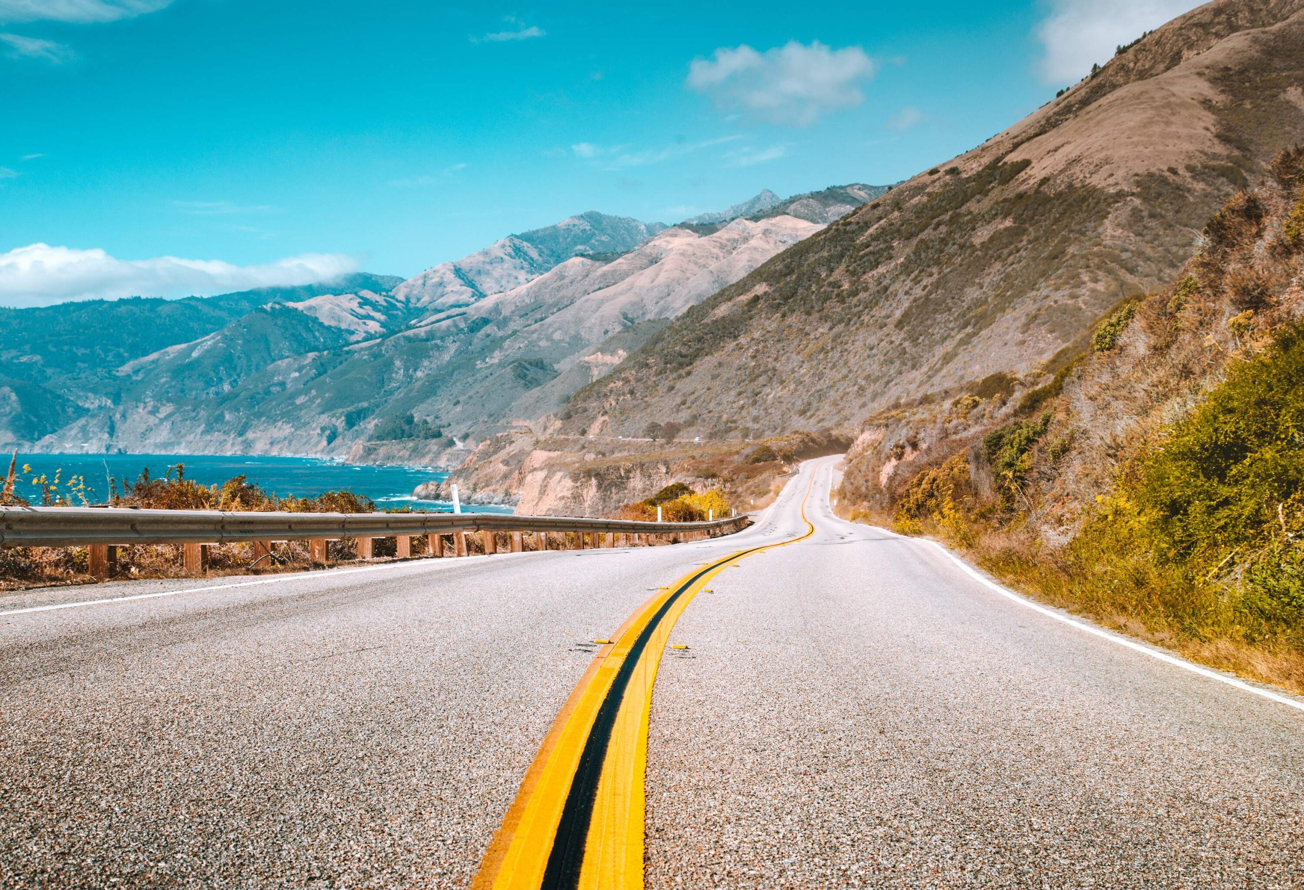 A motorway running along the foothills of a massive mountain range.