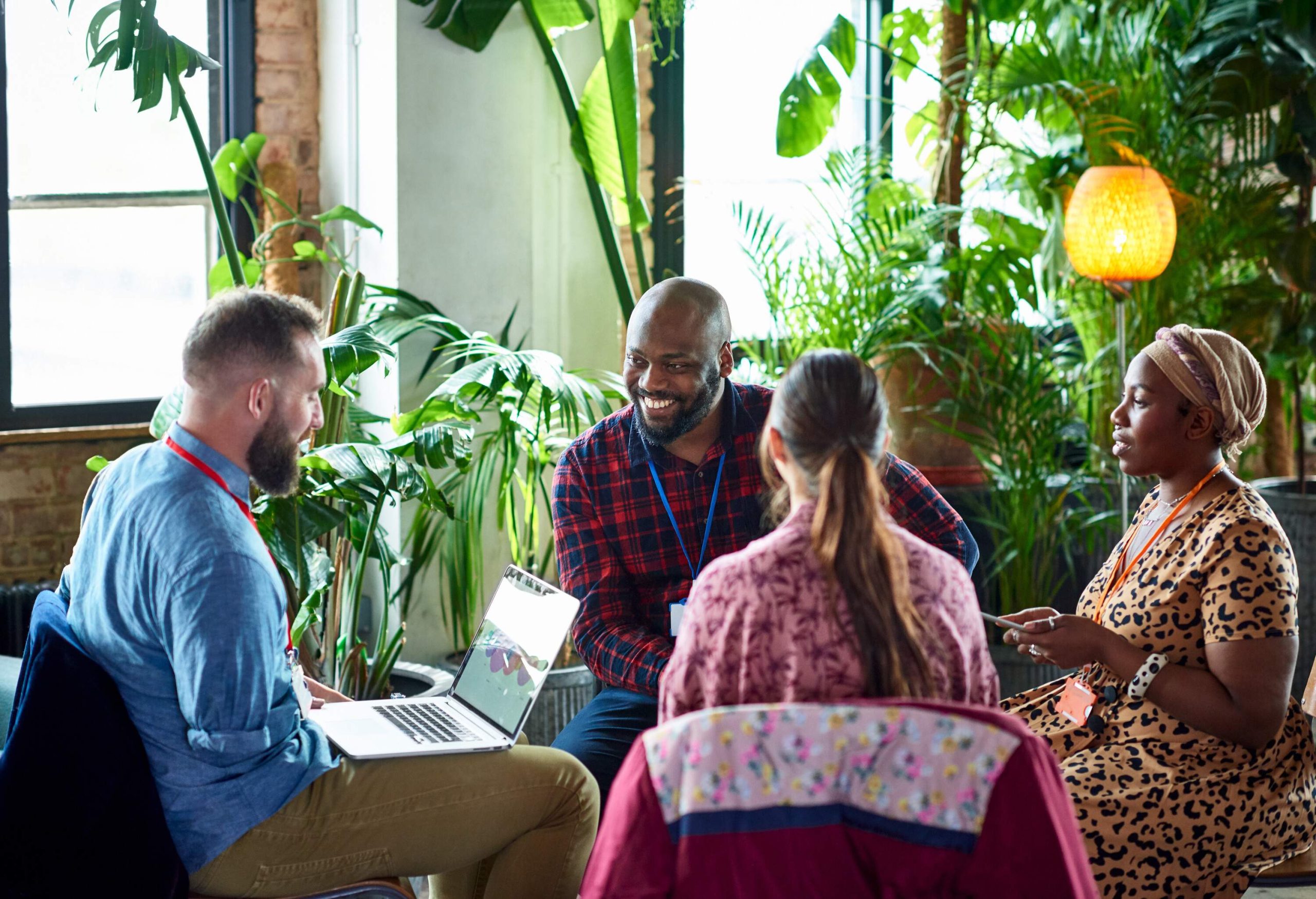 An amputee with a laptop leads a meeting with three other co-workers inside a café with lush foliage.